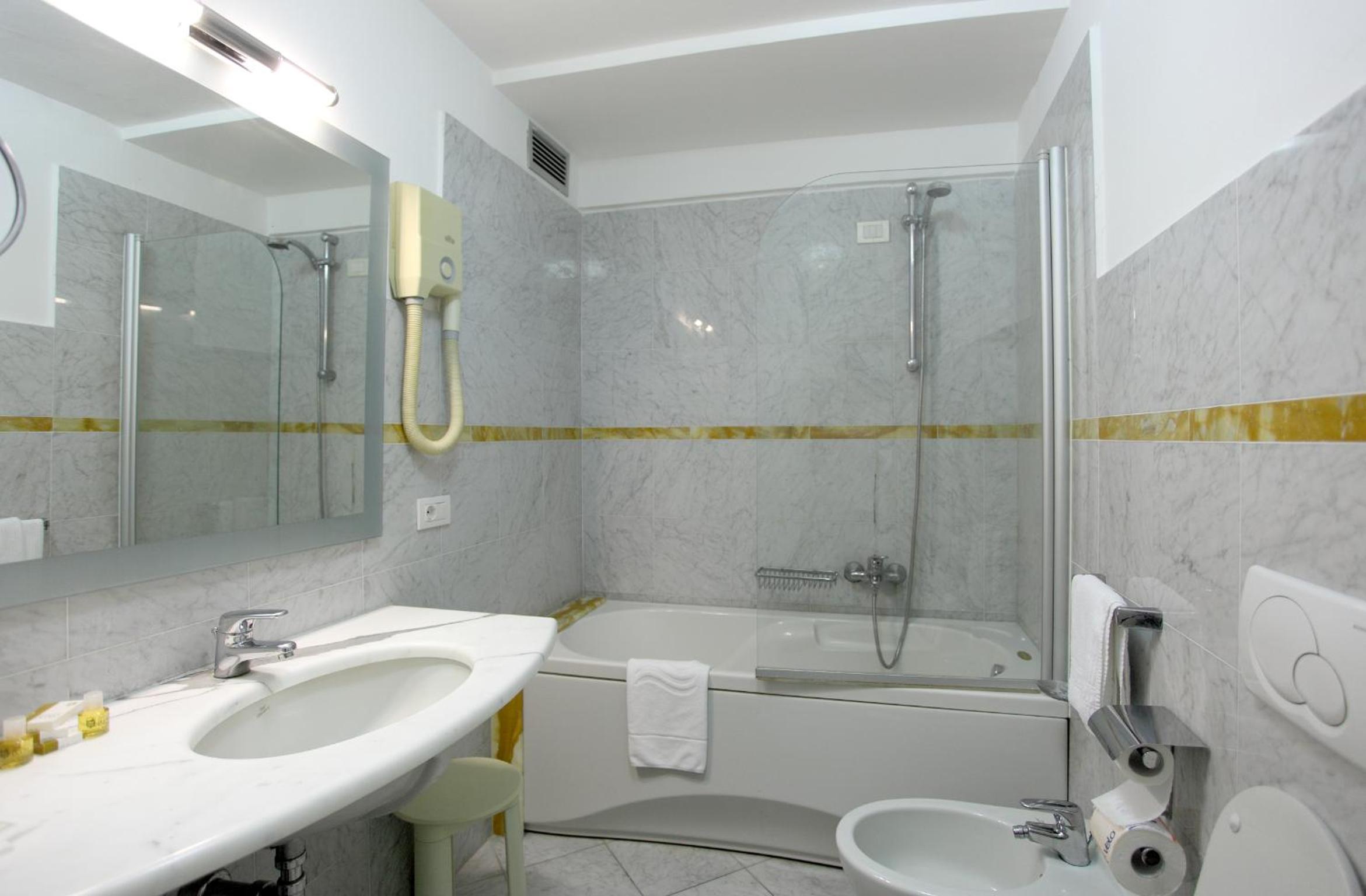 Marble bathroom with a fitted bathtub, overhead shower, wide vanity counter, and bidet.