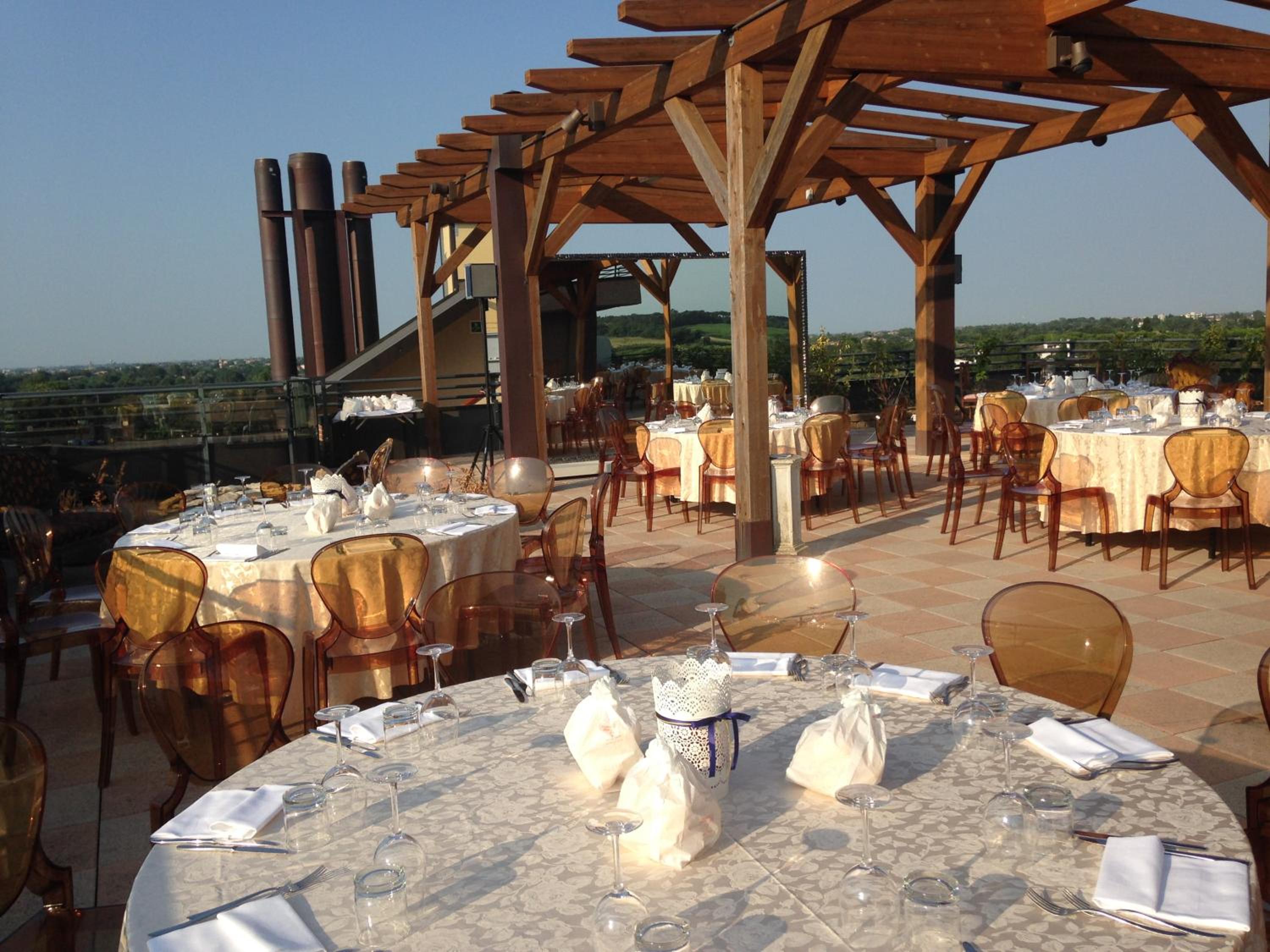 Rooftop terrace under a timber pergola with formal banquet tables, amber chairs, and countryside views.