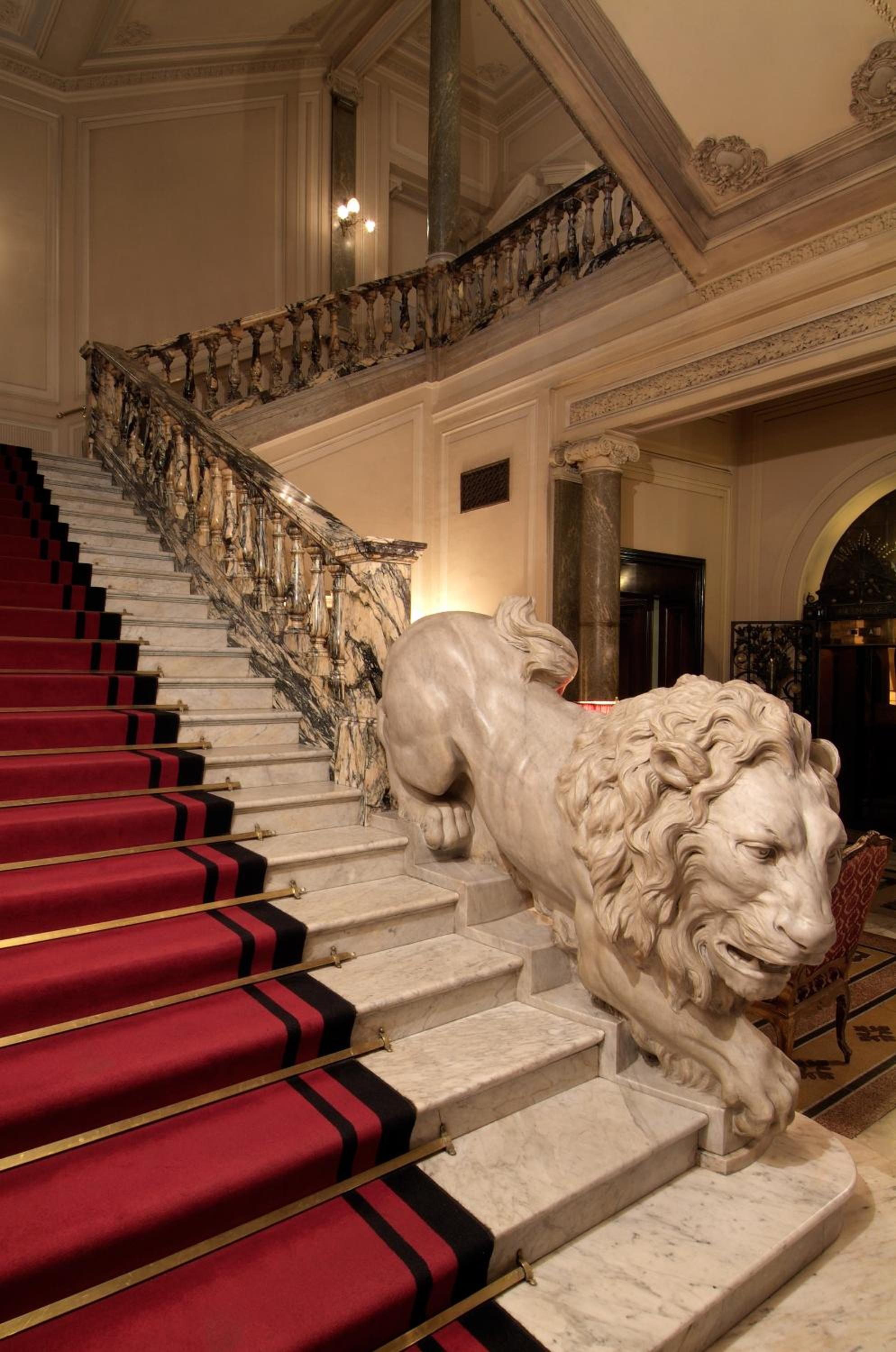 A marble staircase with a red carpet and a large carved marble lion sculpture along the balustrade.
