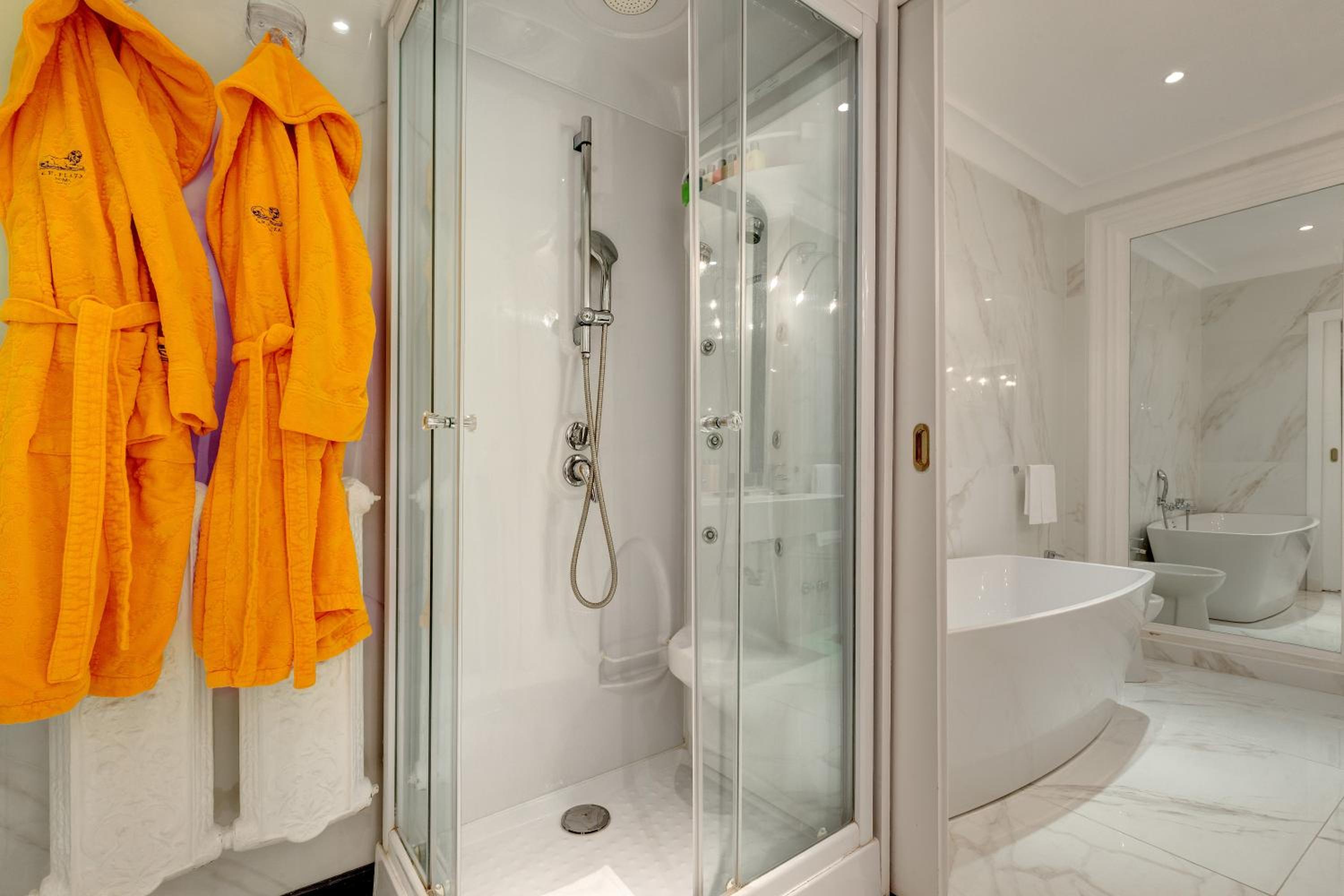A bathroom featuring a glass shower stall, bright yellow bathrobes, and a white freestanding bathtub.