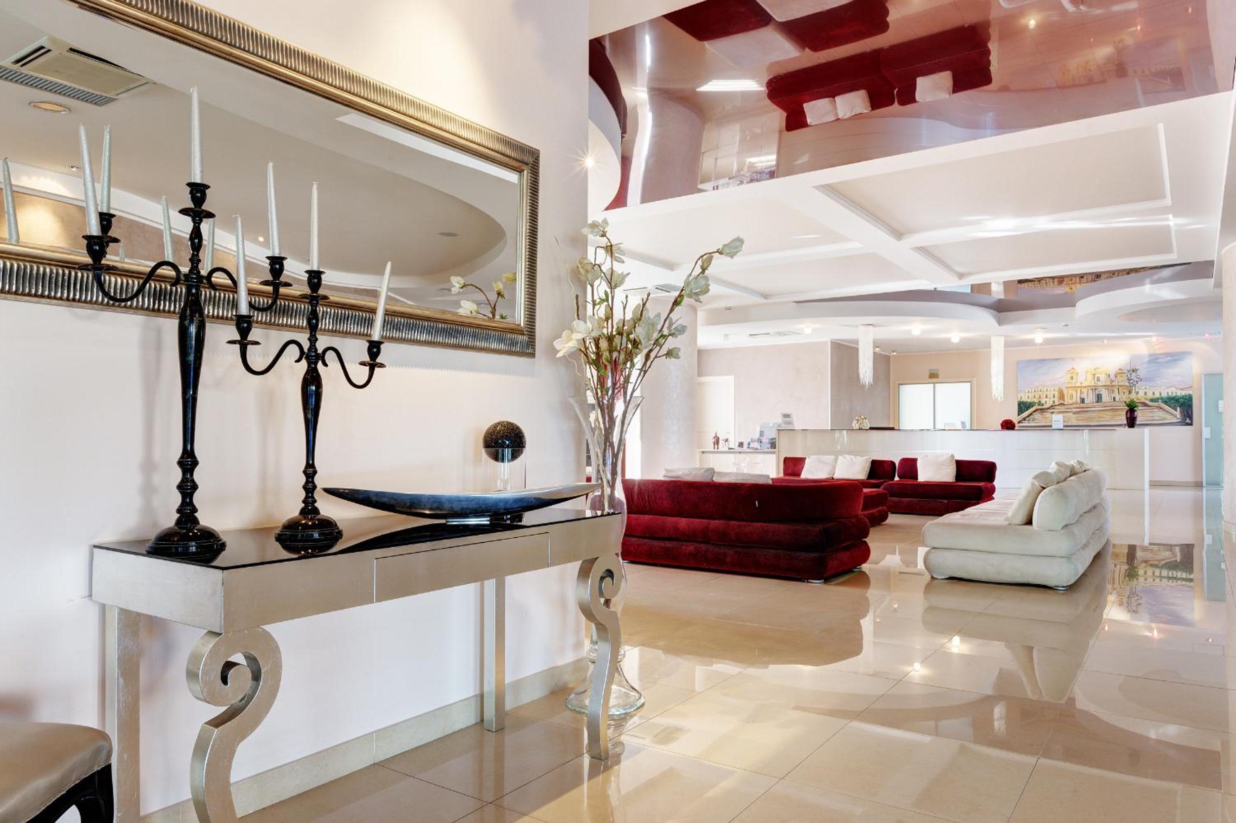 Polished tile lobby with velvet sofas beneath a glossy red ceiling and a mirrored console with candelabras.