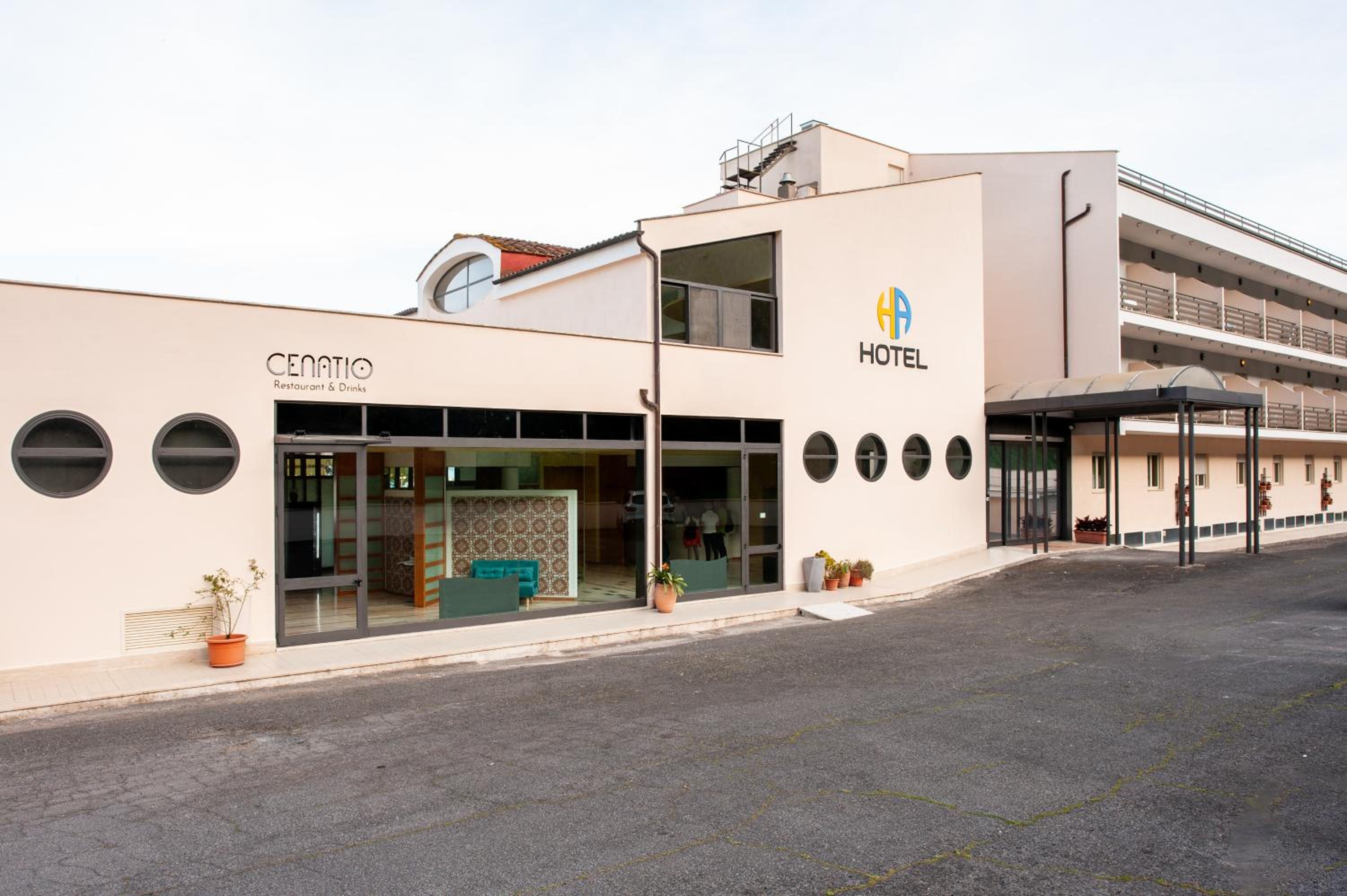 Exterior of HA Hotel featuring a pale facade, porthole windows, and large glass entrance doors.