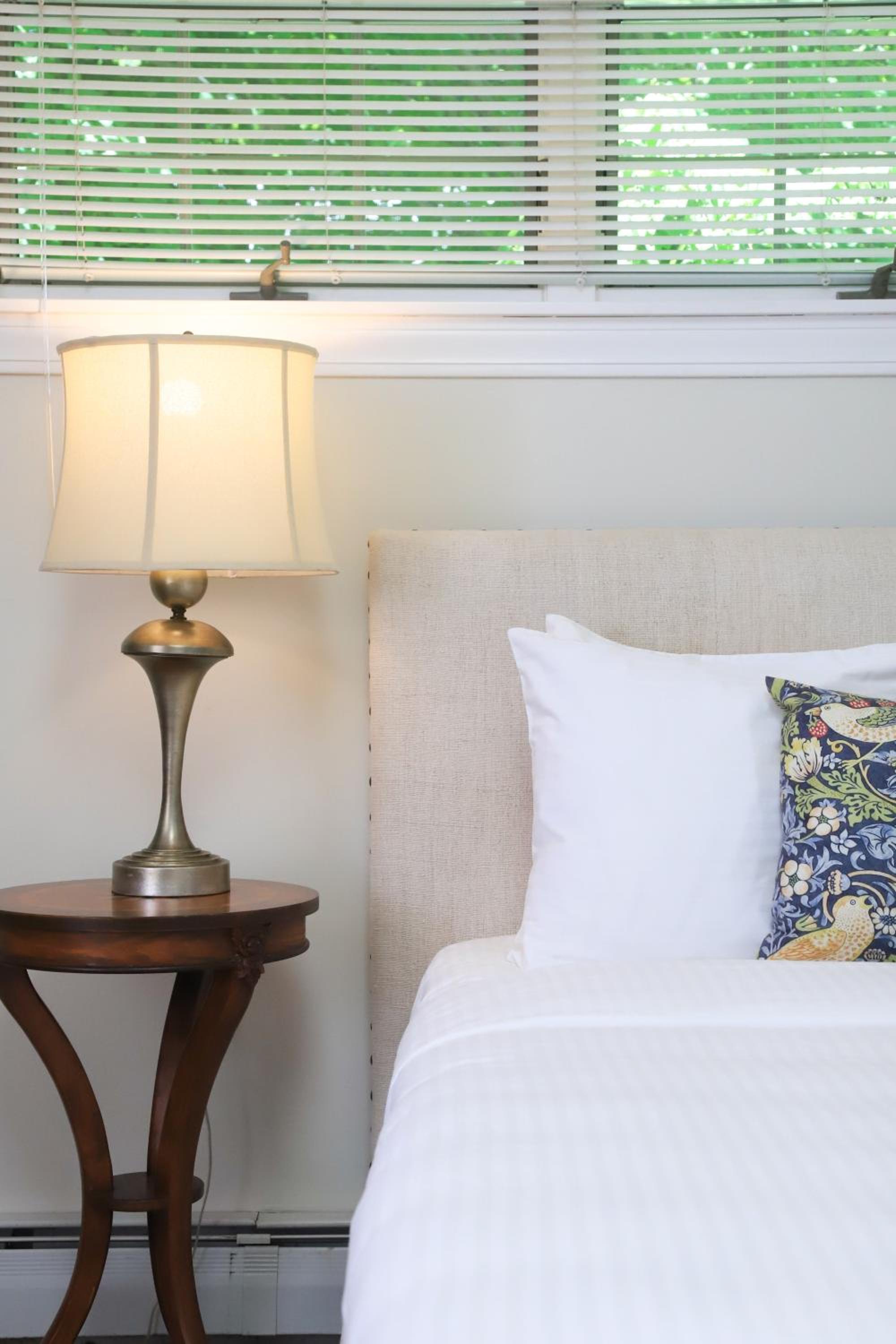 A curved wooden bedside table with a lit brass lamp sits beside a bed with a fabric headboard.