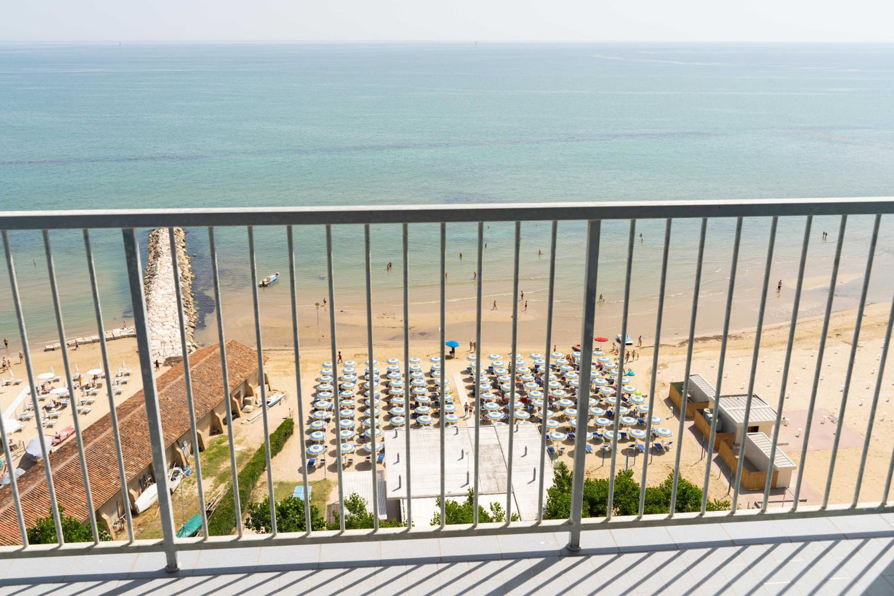 View through a balcony railing looking down onto rows of umbrellas on a sandy beach and the sea.
