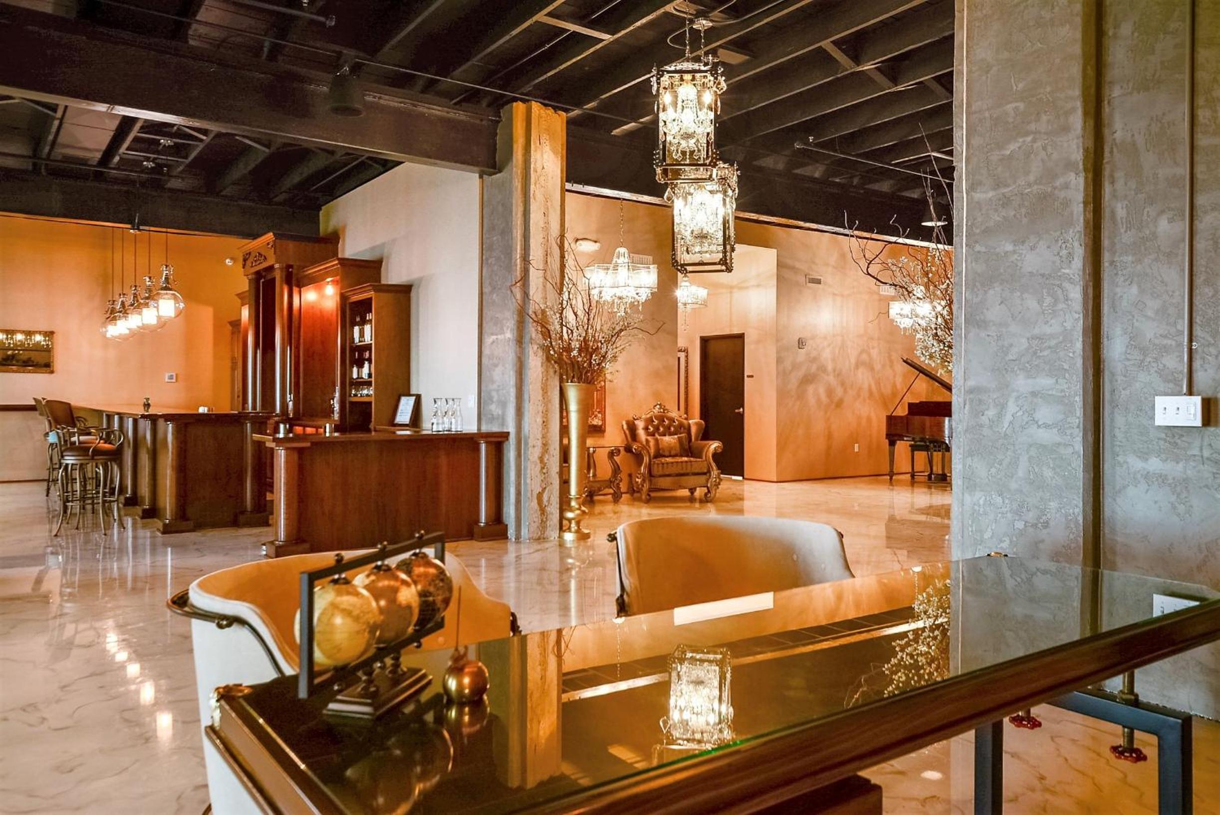 Lobby with polished floors, pendant chandeliers, dark exposed rafters, seating, and a bar counter.