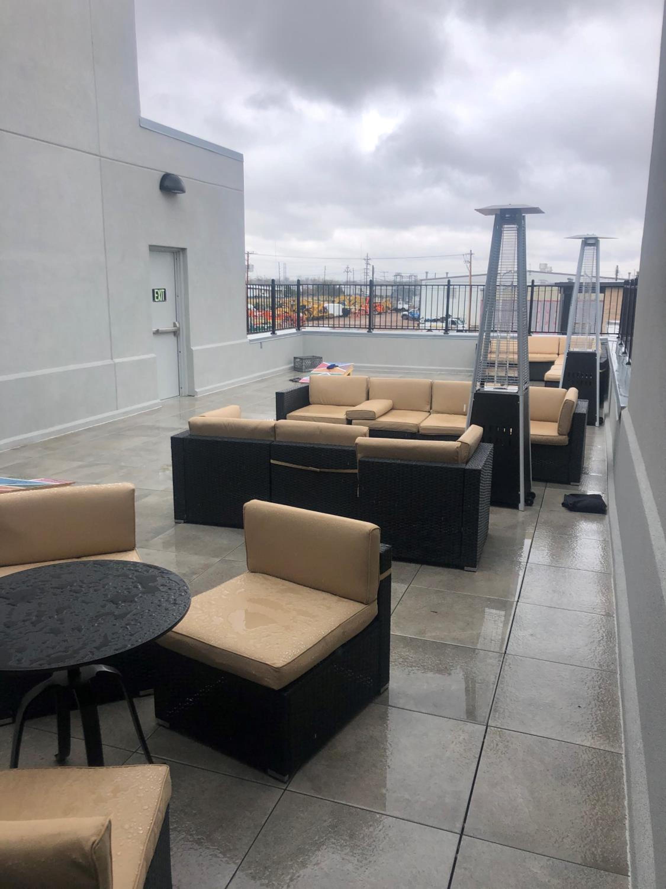 Wet patio tiles lined with dark wicker lounge seating and tall patio heaters beneath an overcast sky.