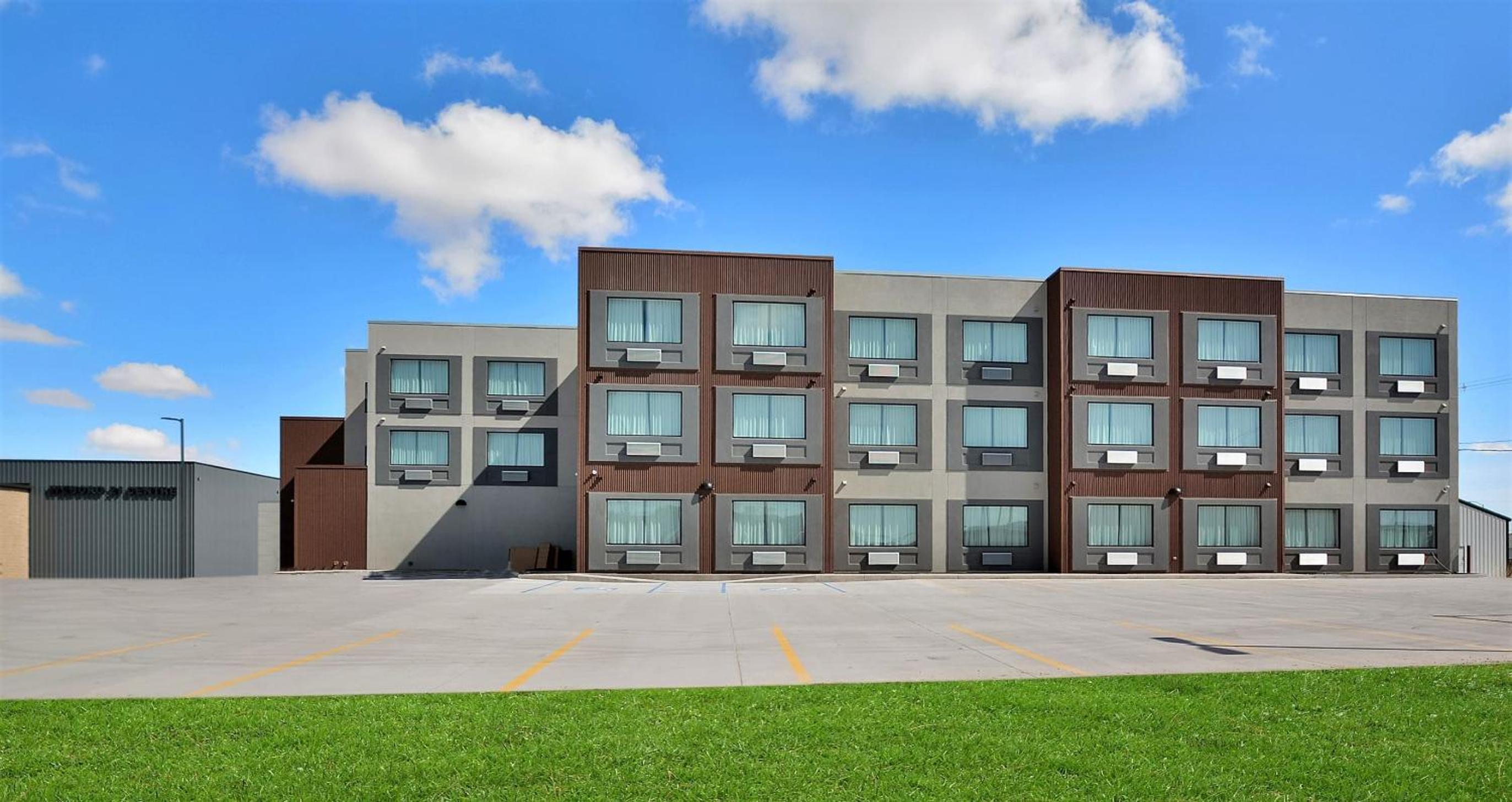 Multistory hotel exterior with brown and gray paneled siding facing an empty concrete parking lot.