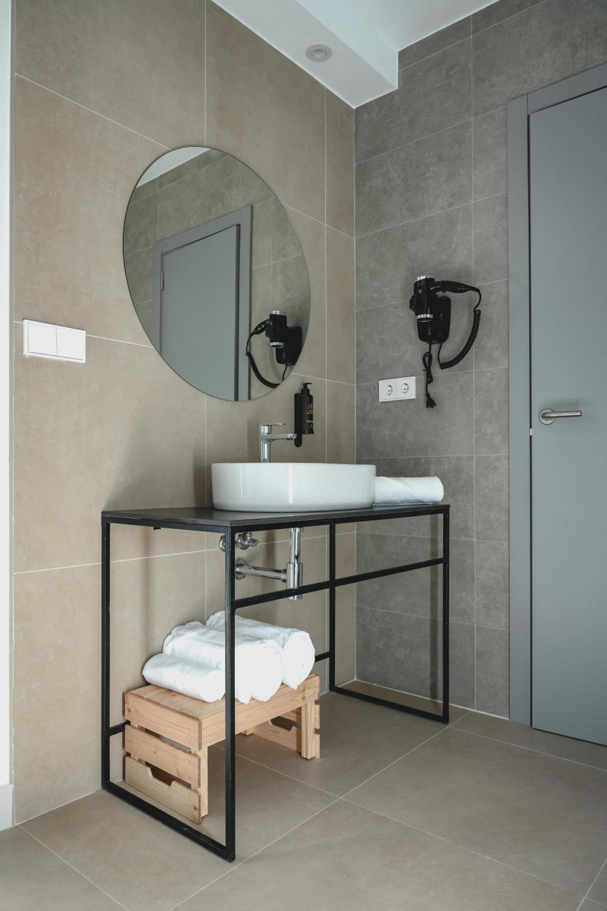 Bathroom with a round mirror, vessel sink on a metal frame, and towels on a wooden step stool.