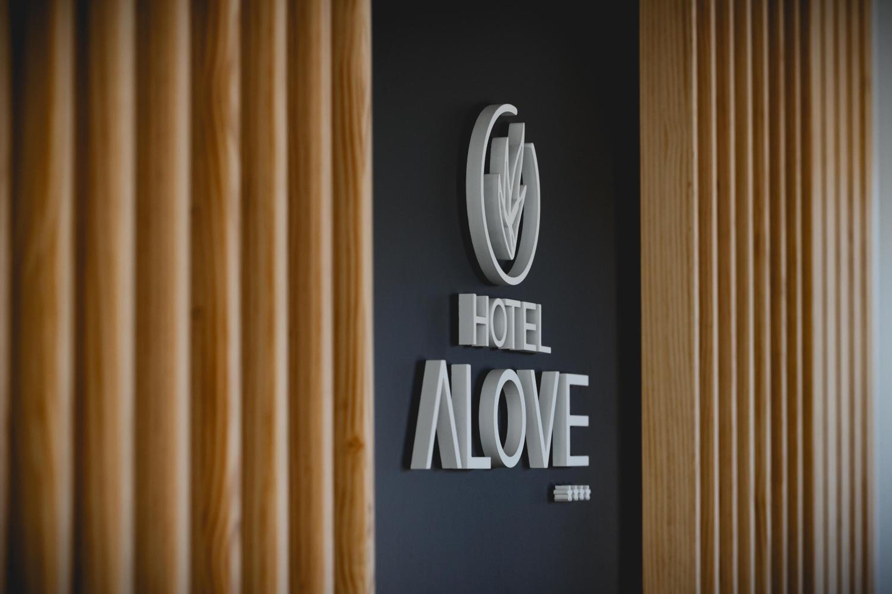 Sign reading Hotel Alove mounted on a dark wall panel framed by vertical wooden slats.