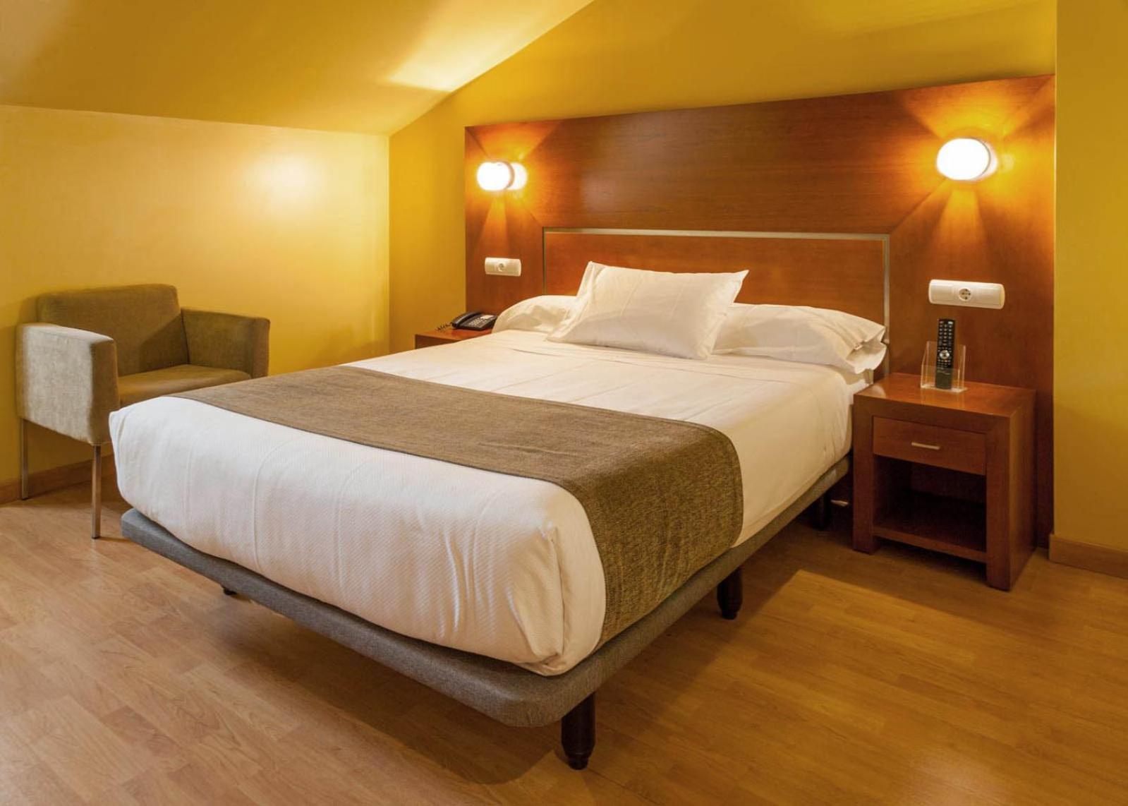 A bedroom under a sloped ceiling with yellow walls, a bed, a wooden headboard, and an armchair.