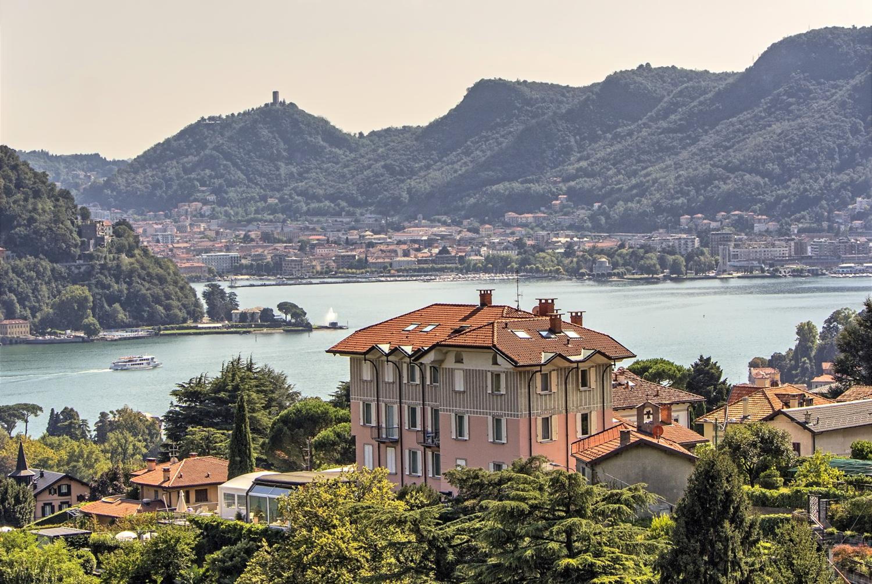 Elevated view of Lake Como, surrounding green mountains, and terracotta-roofed villas of Hotel Asnigo.