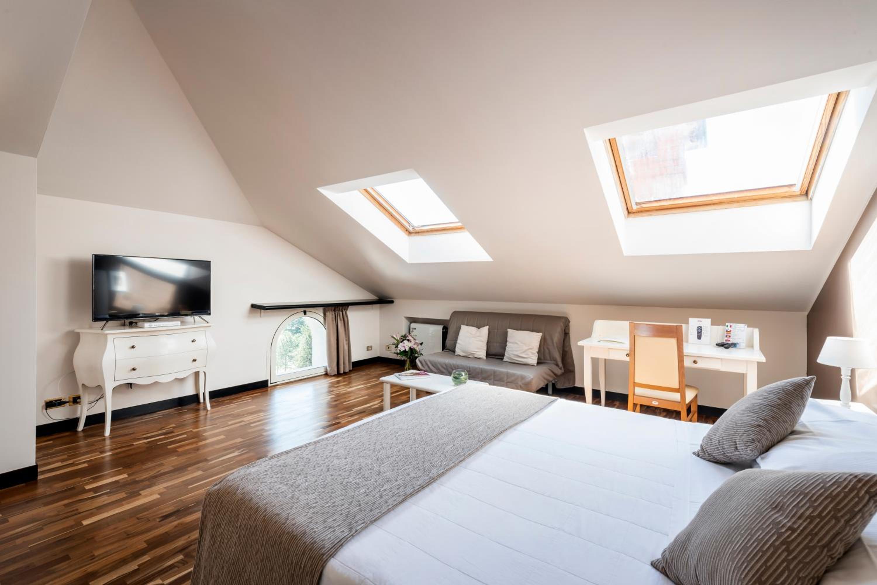 Attic guest room with sloped ceiling, skylights, wood floor, bed, and work desk.