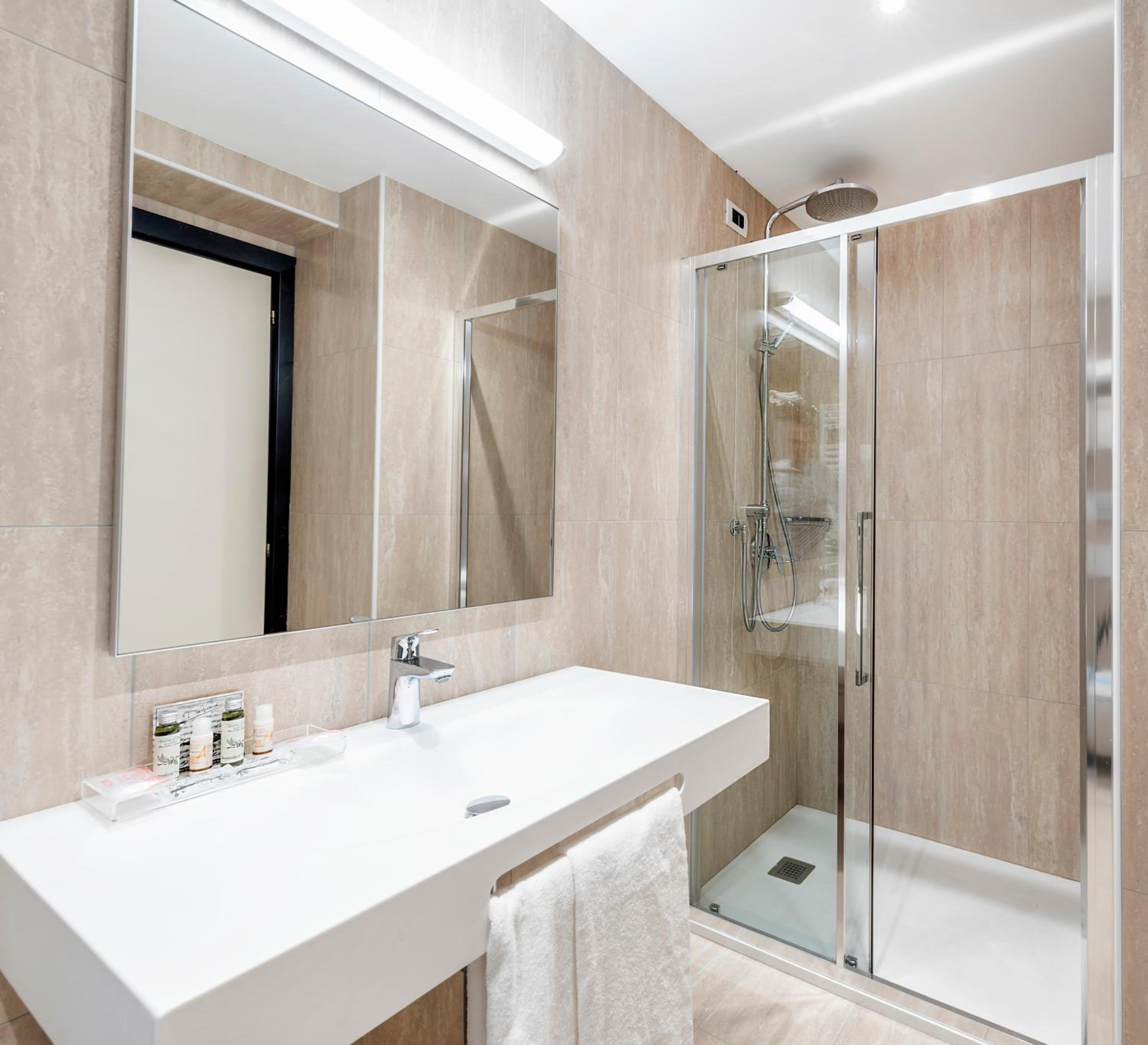 Bathroom with beige tiled walls, a glass walk-in shower, large mirror, and white sink vanity.