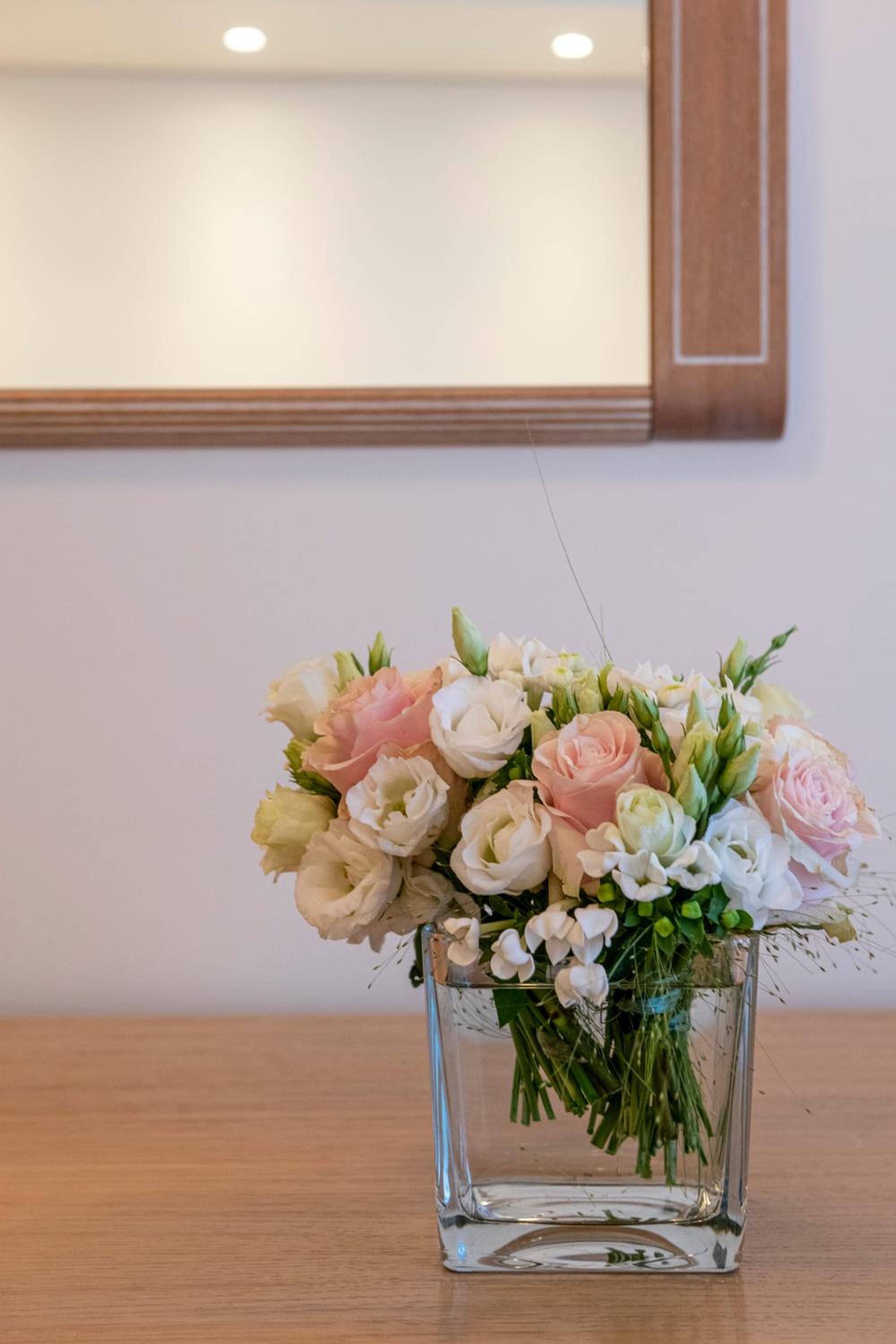 Flower arrangement of pink and white roses in a clear glass vase set on a wooden surface below a mirror.