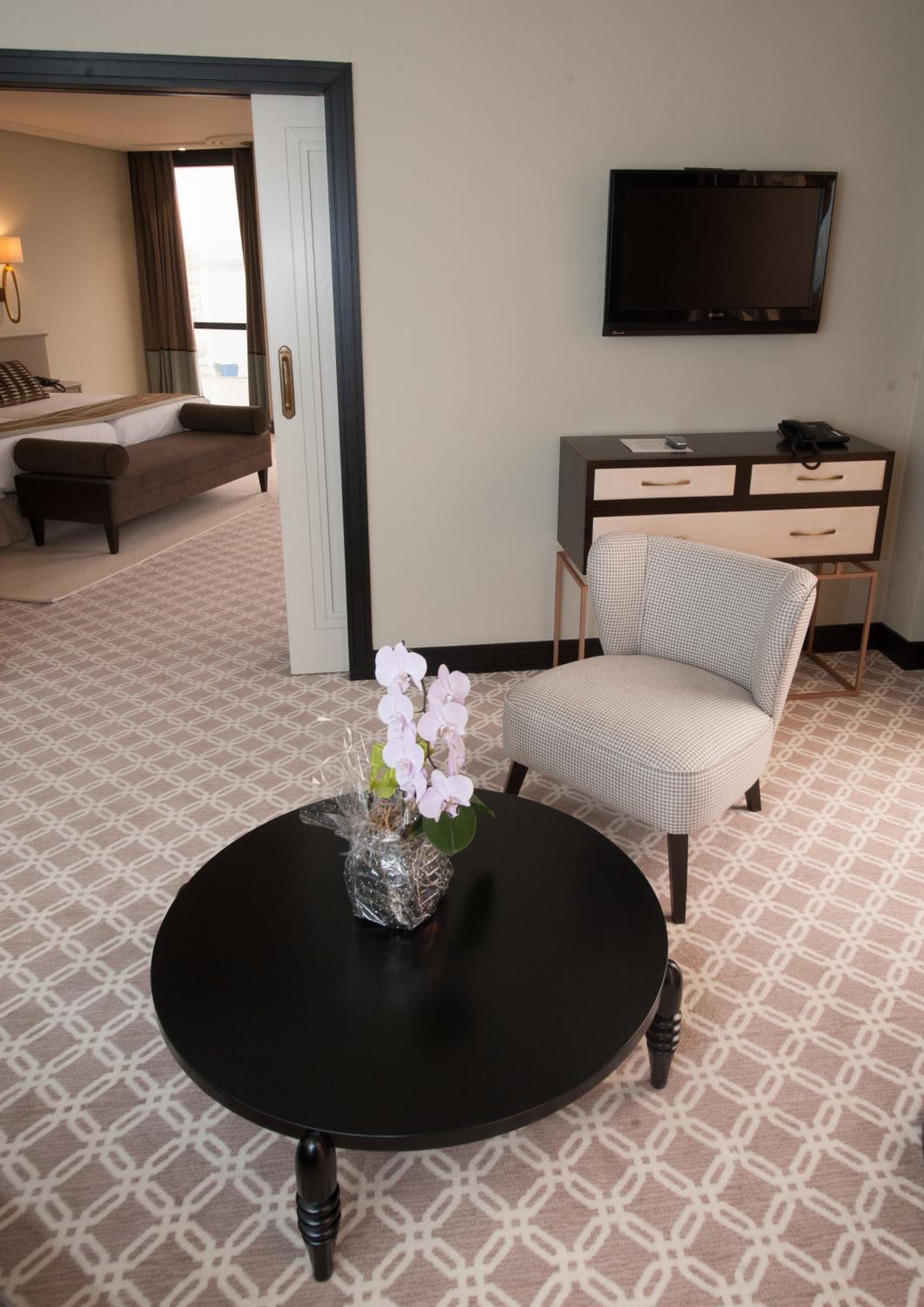 A suite sitting area with patterned carpet, an armchair, and an orchid centerpiece on a black round table.