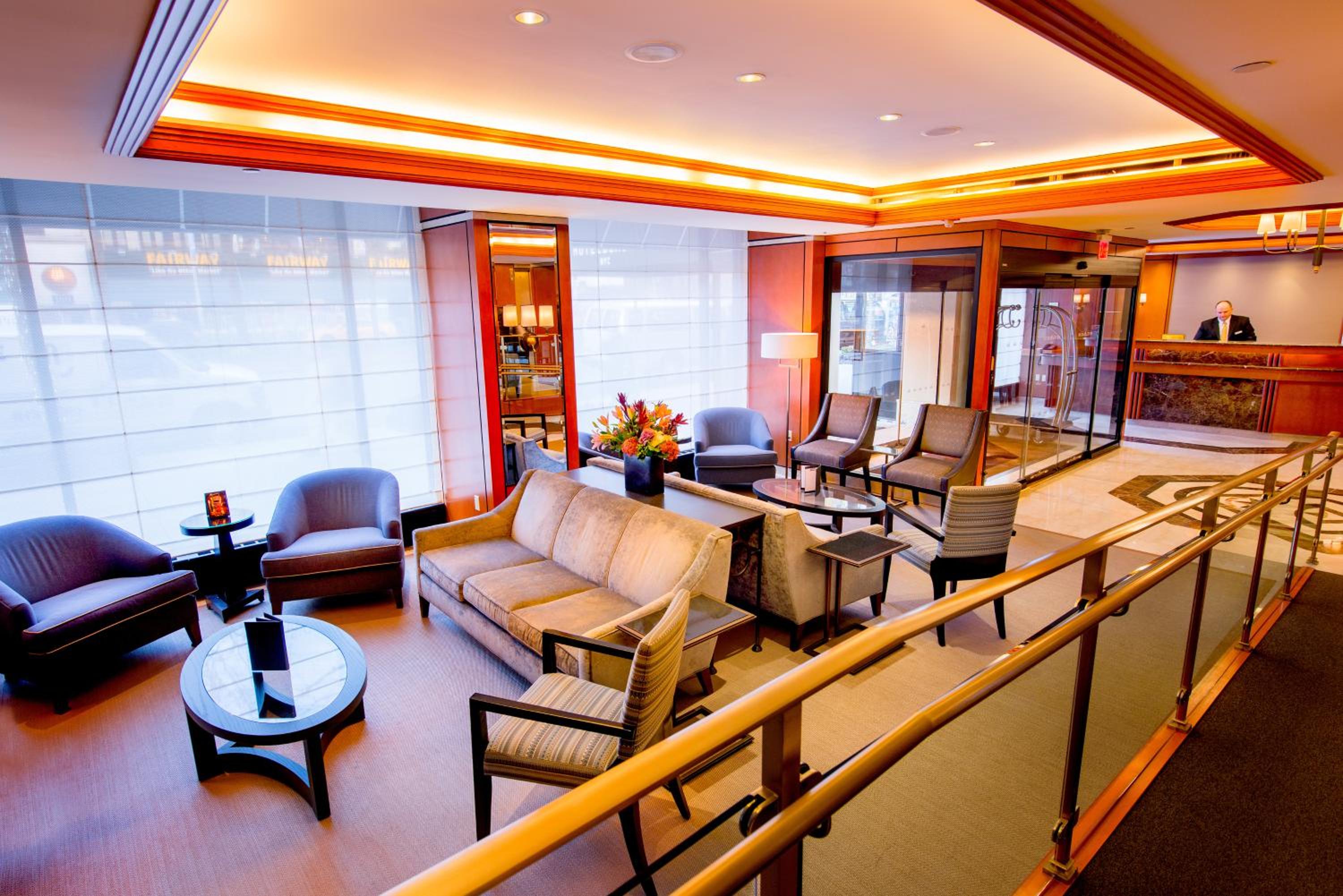 Lobby lounge with plush armchairs, a coffee table, and a reception desk beneath warm ceiling lighting.
