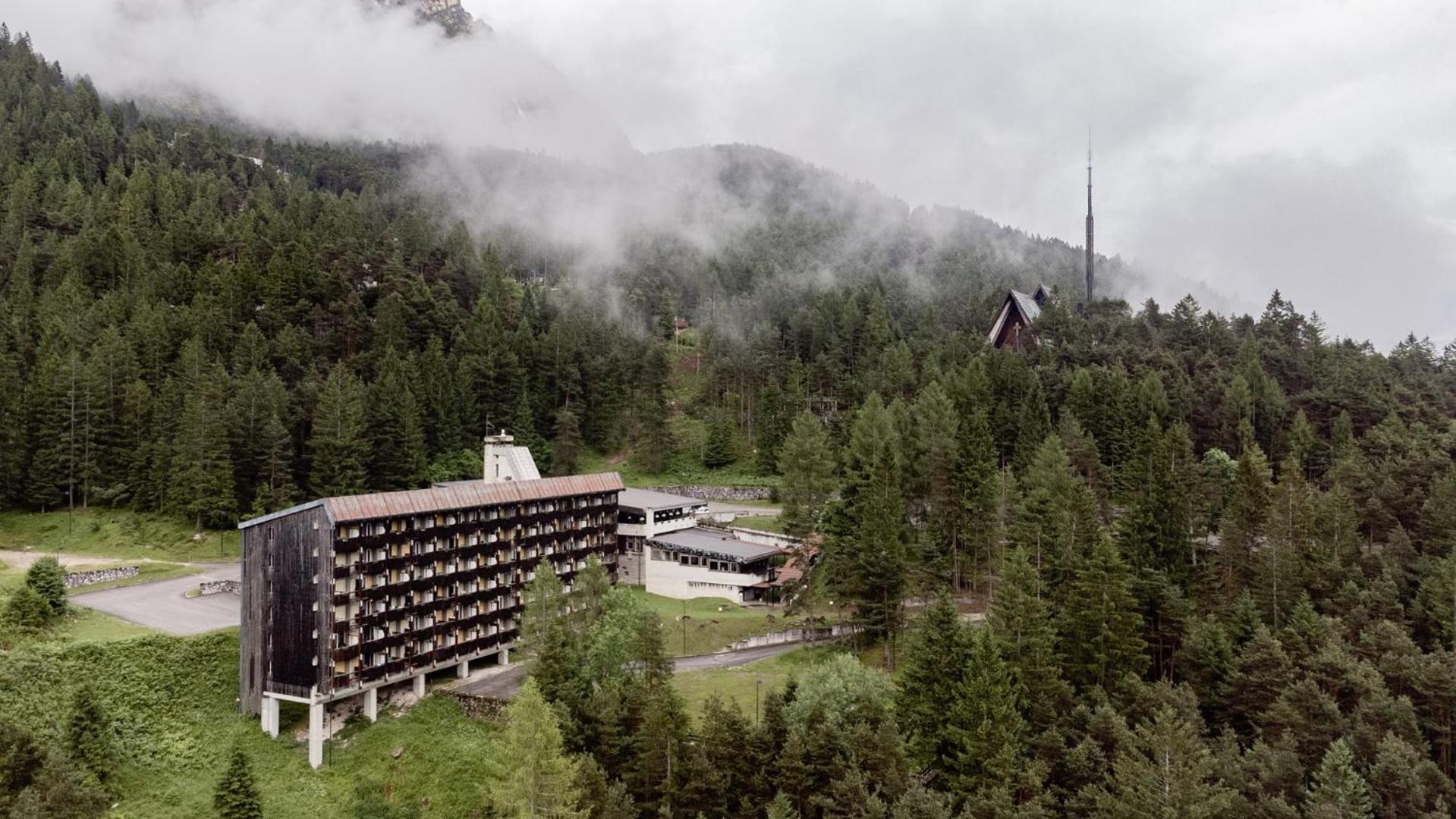 An aerial view of Hotel Boite set against a pine-covered hillside shrouded in low fog.