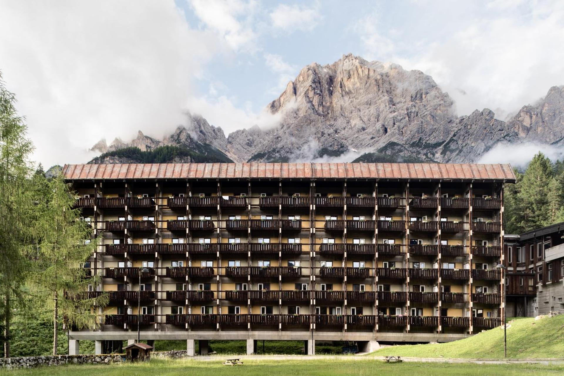 A multi-story lodge facade with rows of wooden balconies stands before a towering rocky mountain.