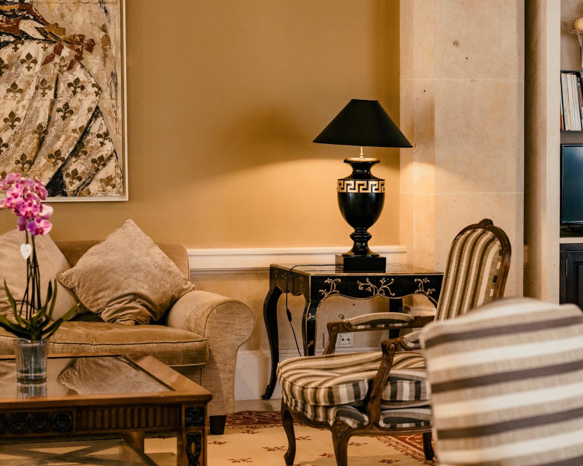 A lounge corner with a striped armchair, a velvet sofa, an orchid, and a classical black urn table lamp.