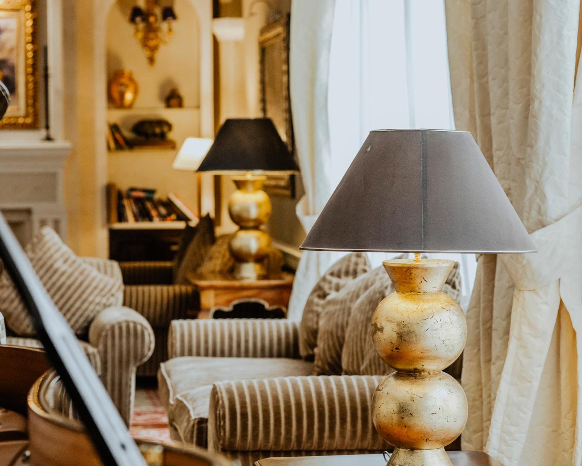 A sitting area with striped armchairs, draped curtains, and a golden stacked-sphere table lamp.