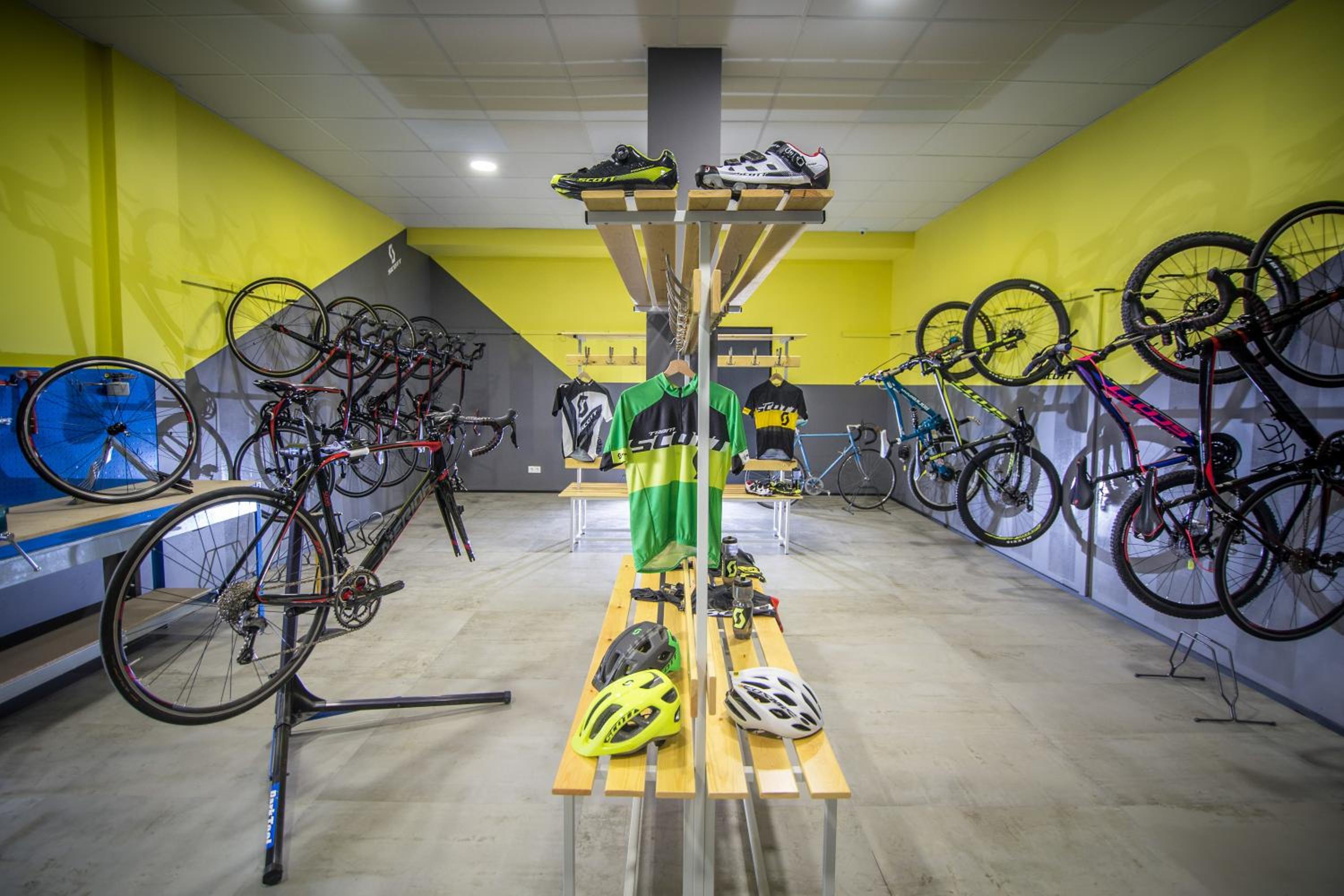 A bicycle storage room with bikes mounted along yellow walls, display racks, helmets, and jerseys.