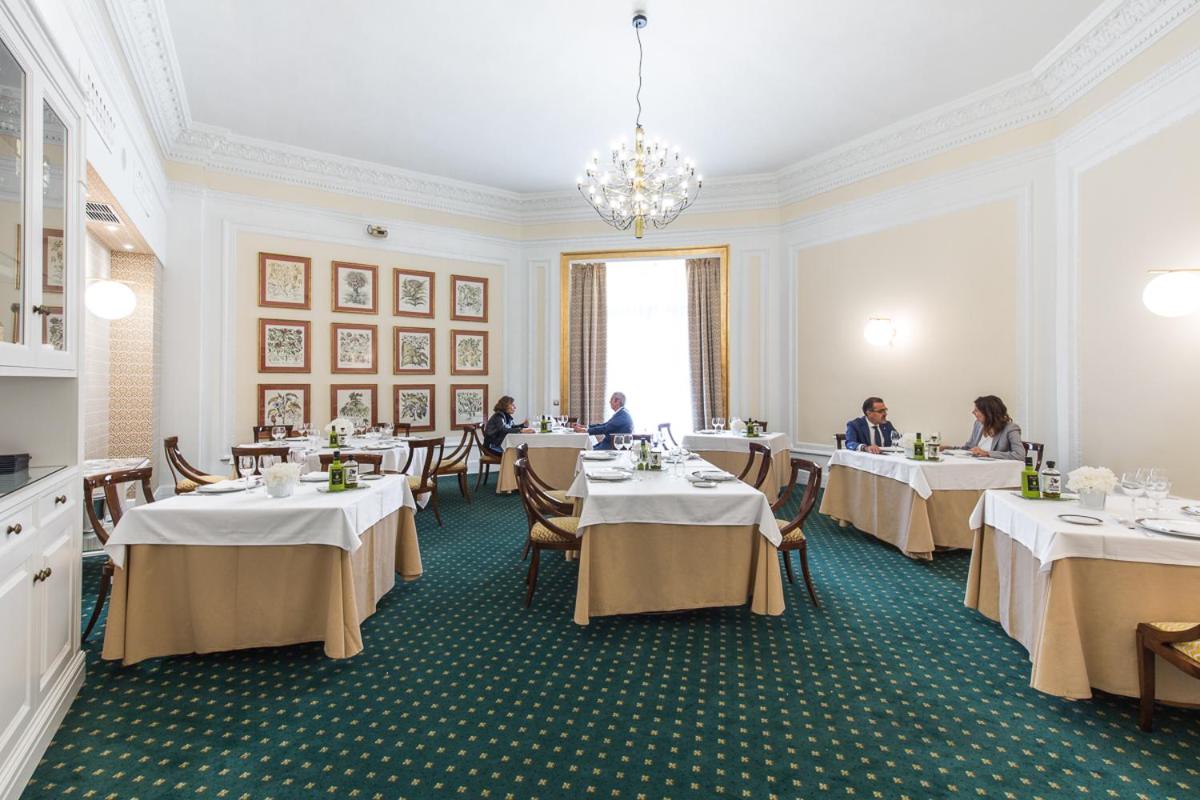 A dining room with green patterned carpet and framed prints on cream walls shows diners at draped tables.