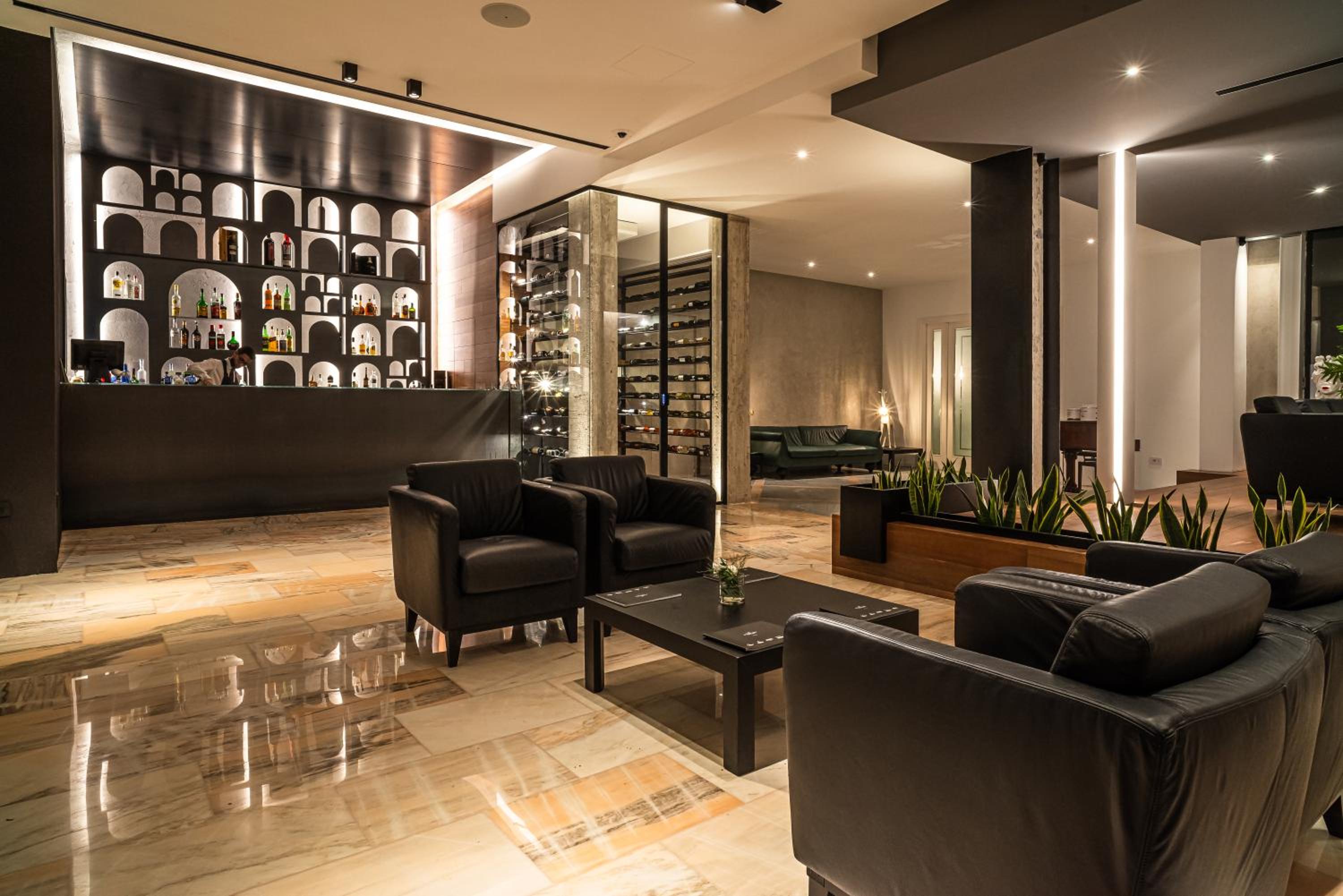 A lounge and bar area with polished marble floors, dark leather armchairs, and an illuminated wine display.