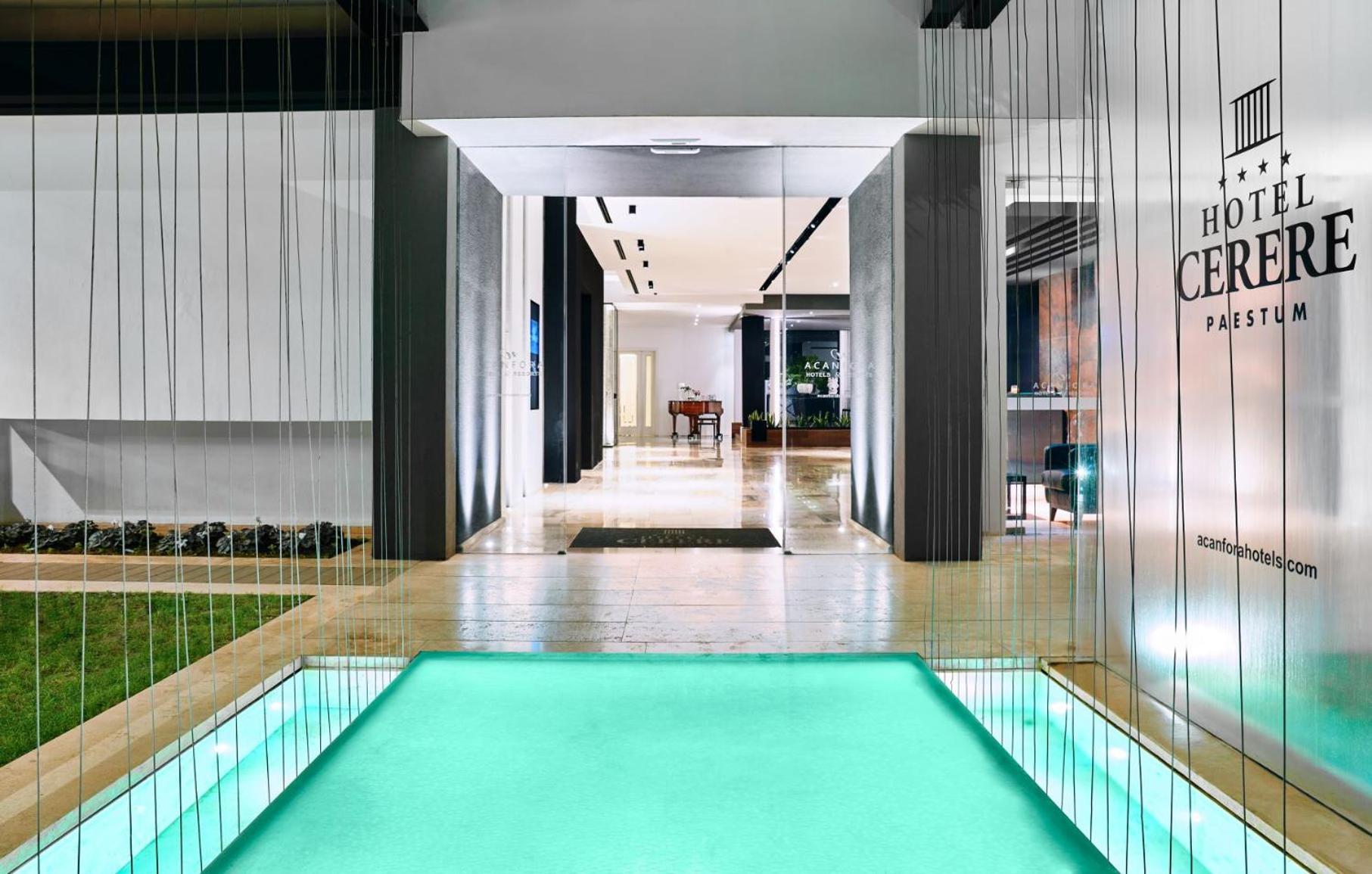 An illuminated turquoise water feature leading into the glass-walled entrance of the building.
