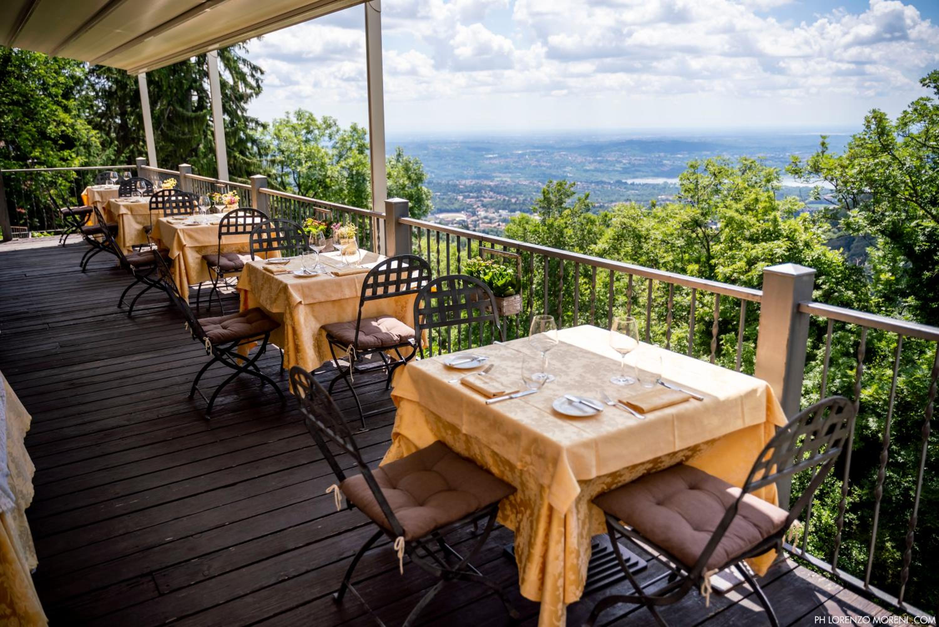 Dining tables set with cloth covers line a covered wooden deck terrace overlooking a forested hillside and the valley.