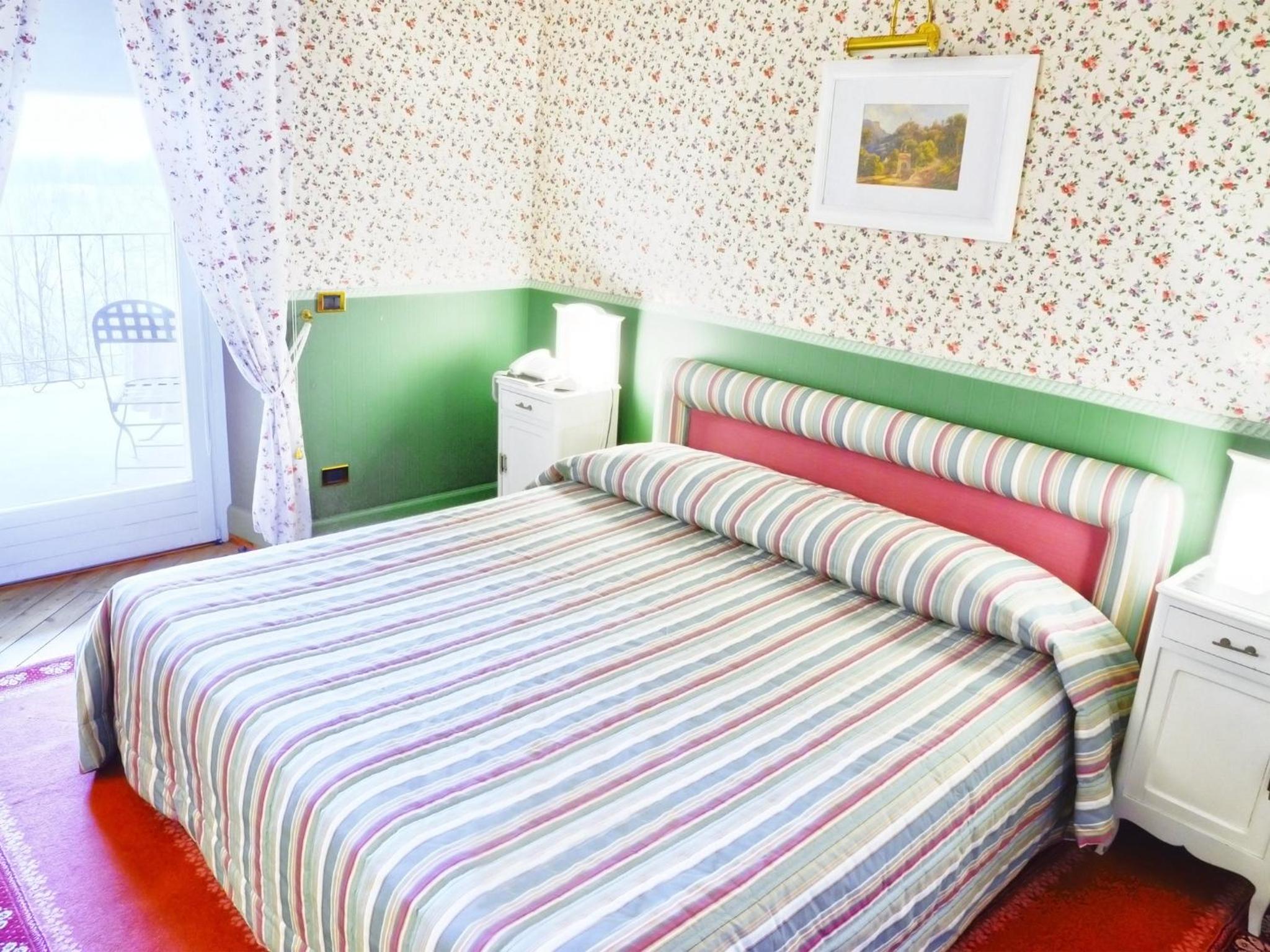 A bedroom at Hotel Colonne features floral wallpaper, green wainscoting, and a bed with a striped spread.