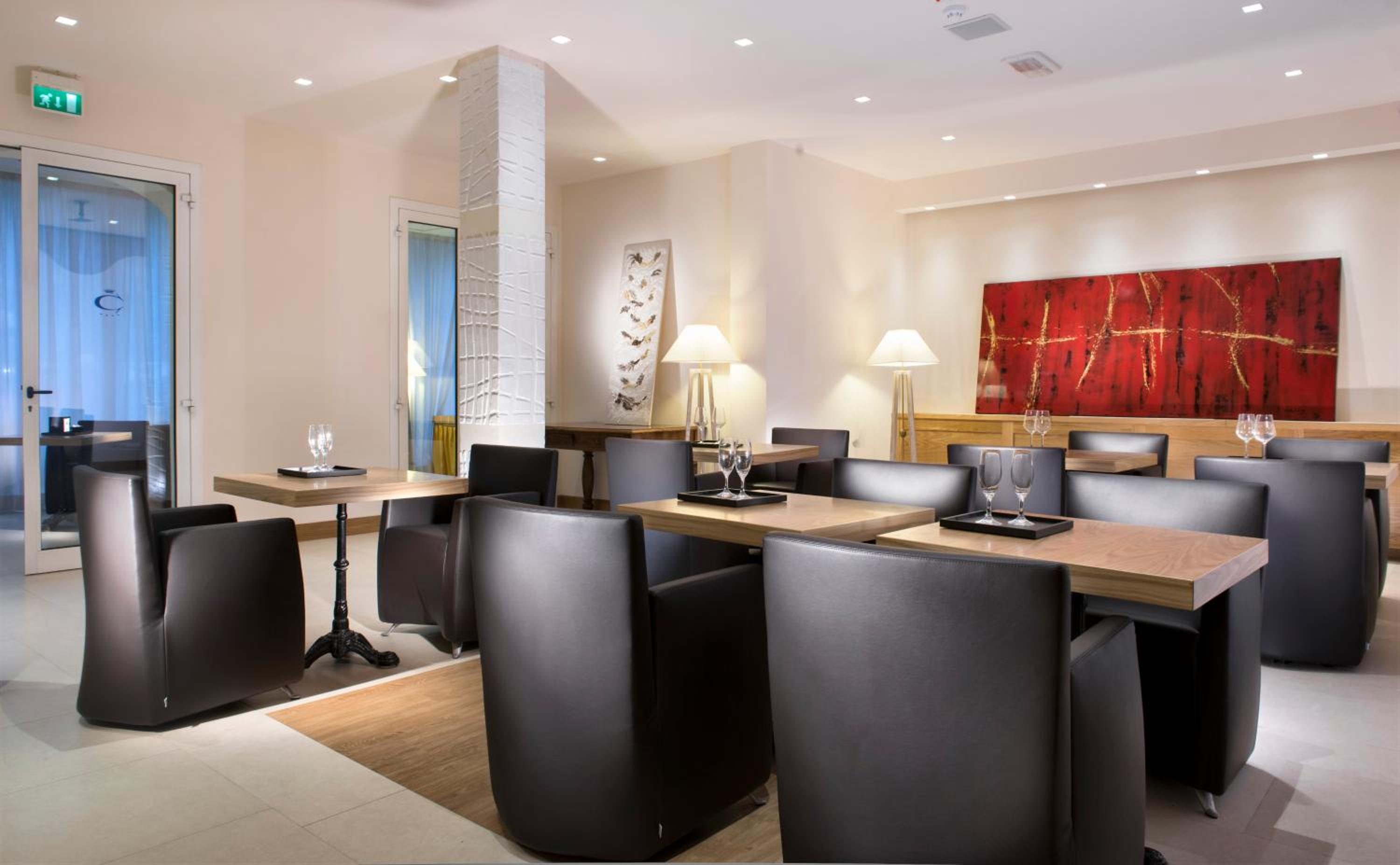 Indoor dining area with dark leather armchairs, wooden tables set with wine glasses, and textured red wall art.