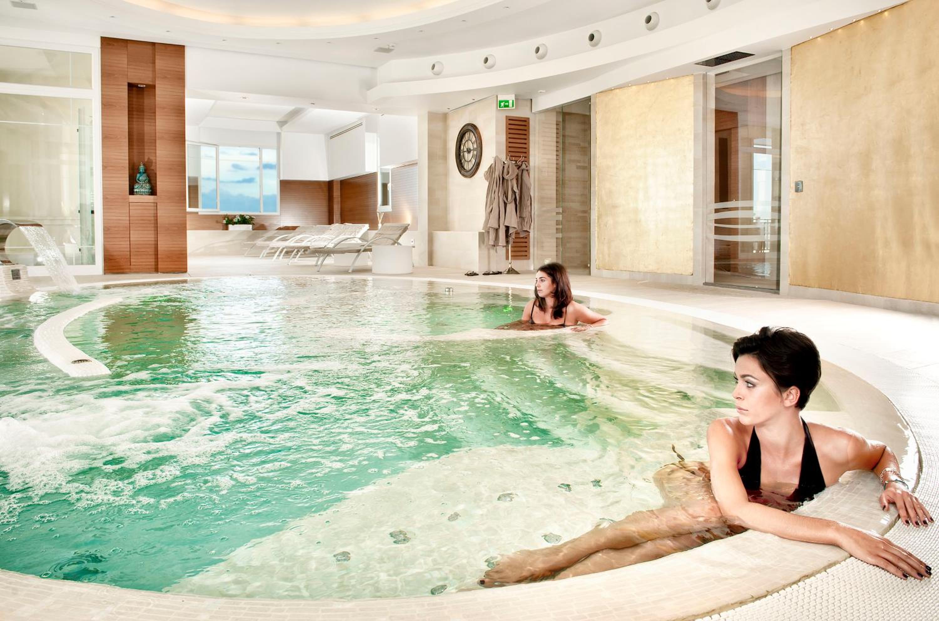 Indoor spa pool with gentle water features and women resting along the curved tiled edge.