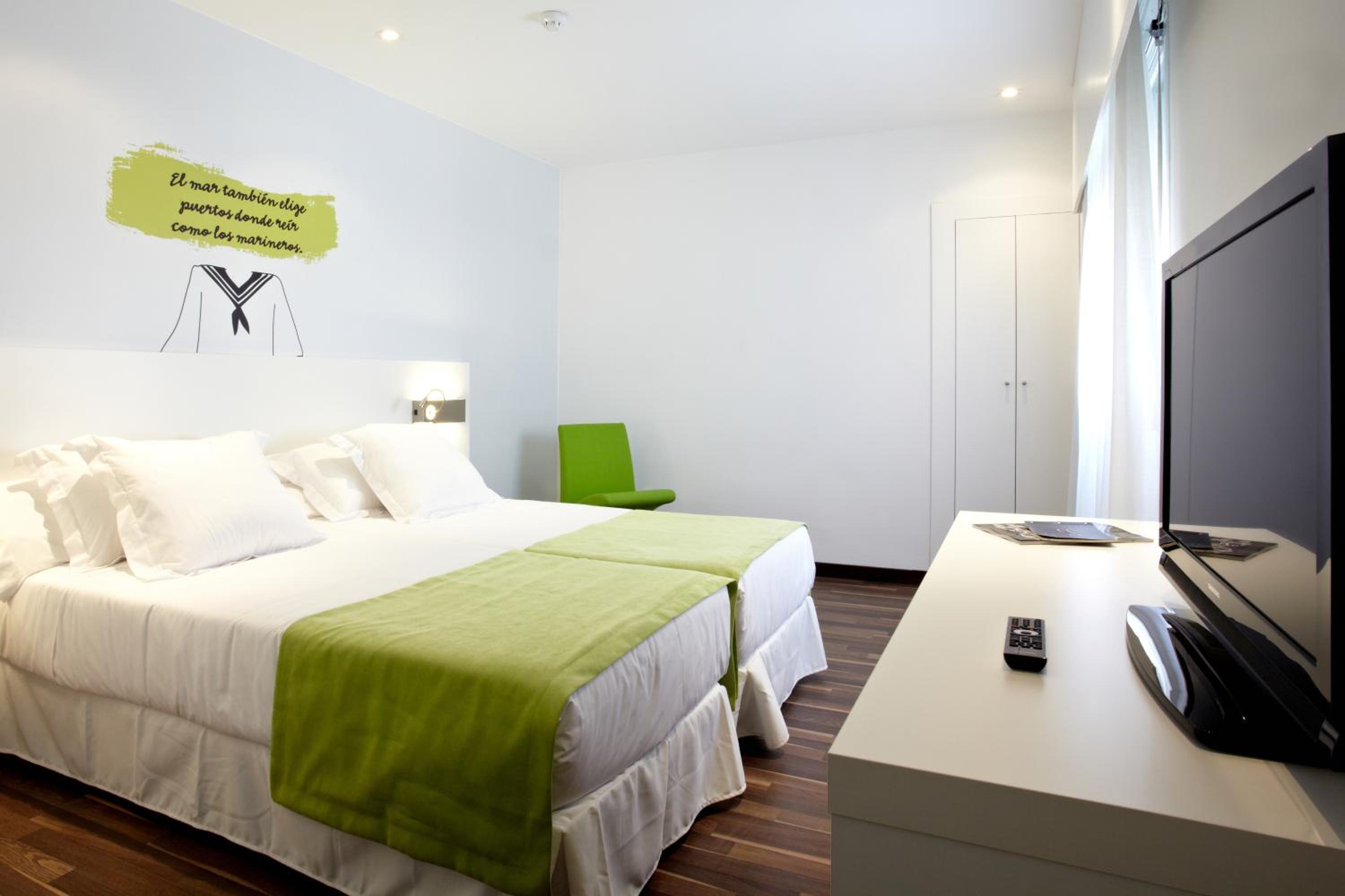 Guest bedroom featuring beds with green runners, a television on a white console, and light blue walls.