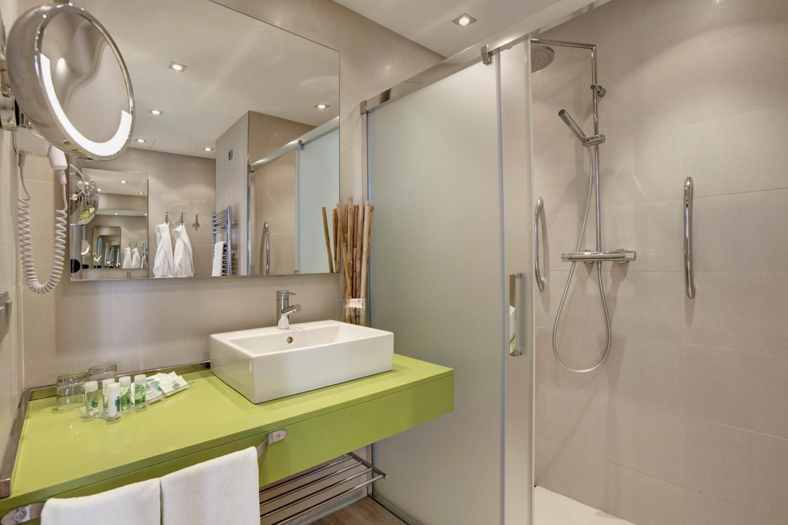 Bathroom with a lime-green vanity, square vessel sink, round lit mirror, and tiled walk-in shower.