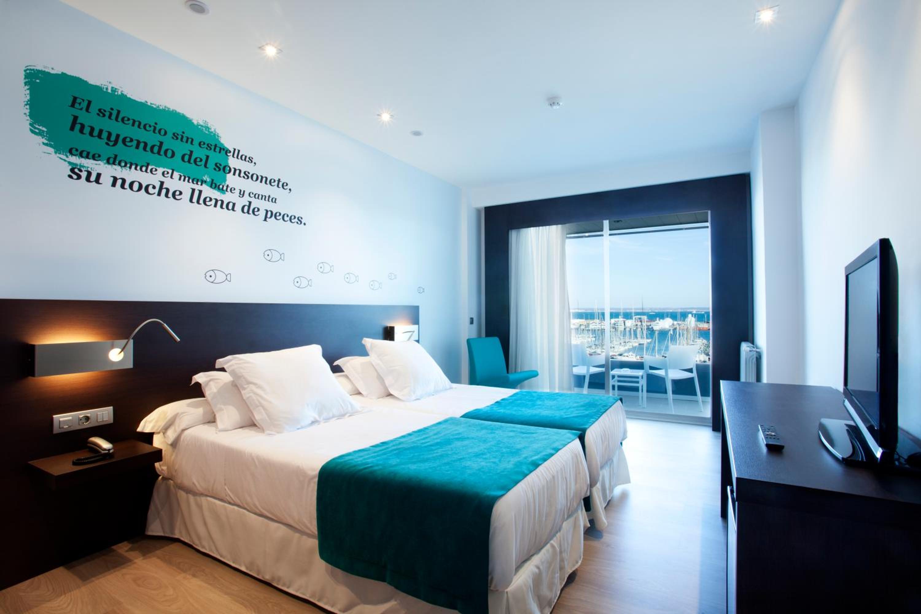 Bedroom with teal bed accents, wall script, and sliding glass doors looking out toward boats in the harbor.