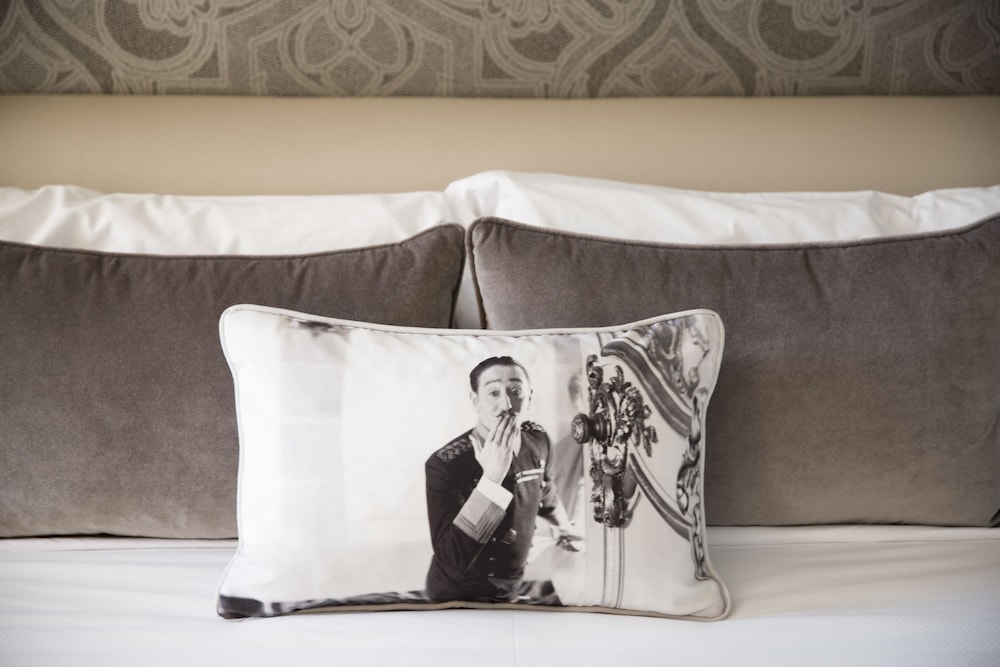 A decorative pillow printed with a black-and-white portrait resting on a bed against brown velvet cushions.