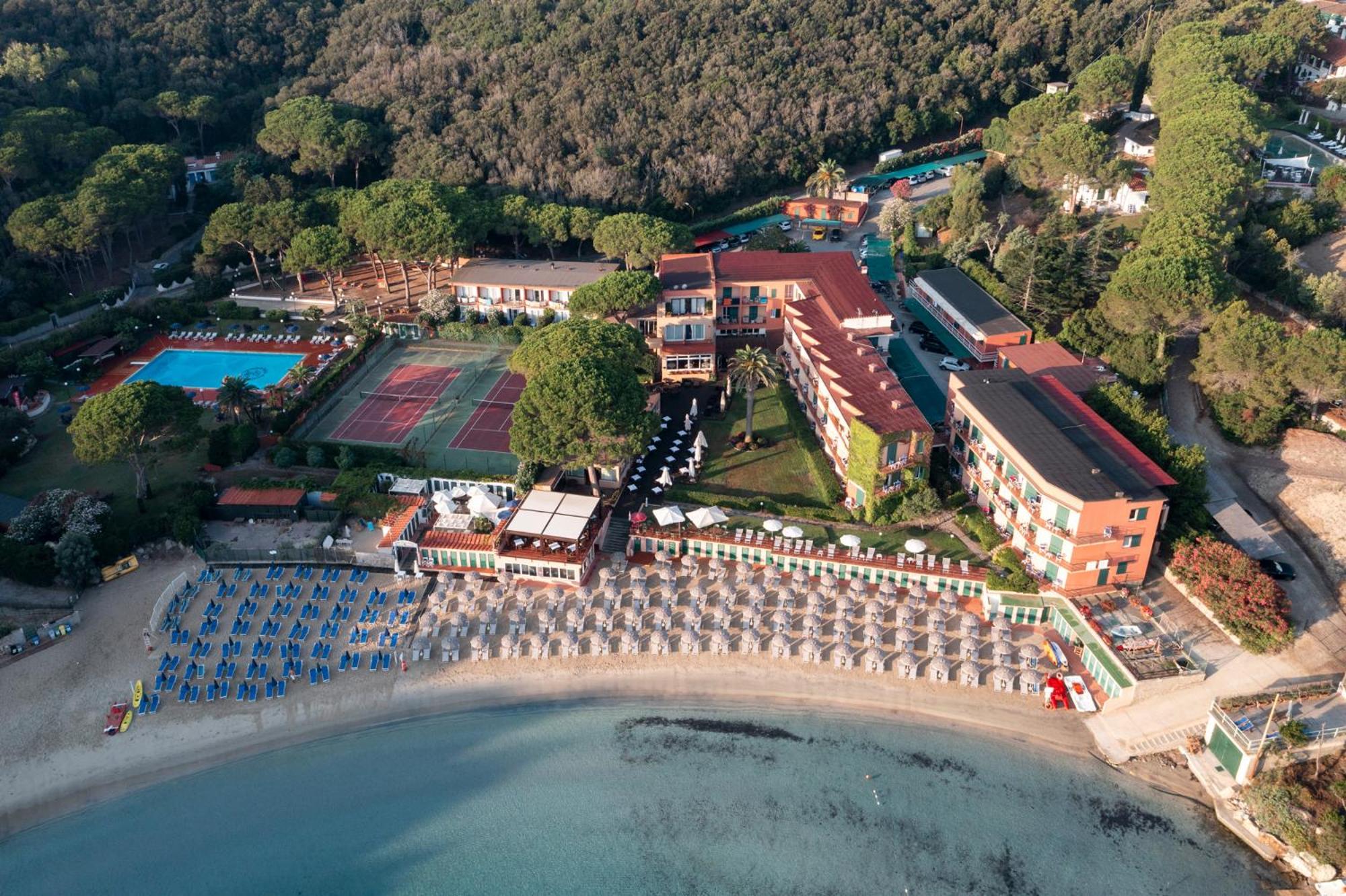 Aerial view of Hotel Desiree with tennis courts, a pool, and a beach along a quiet bay.