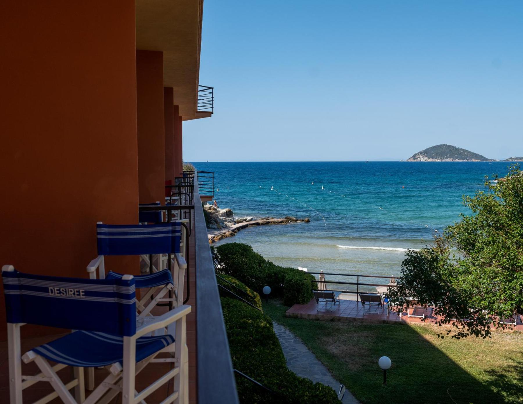 Director chairs on a hotel balcony overlooking a lawn and the open blue sea.