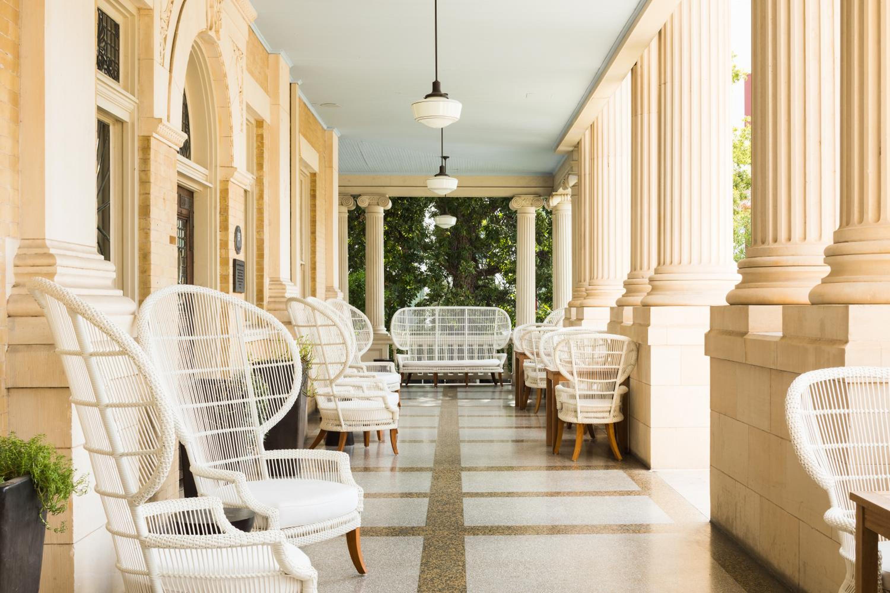 Covered veranda with tall fluted columns, pendant lamps, and white wicker armchairs on tiled floors.
