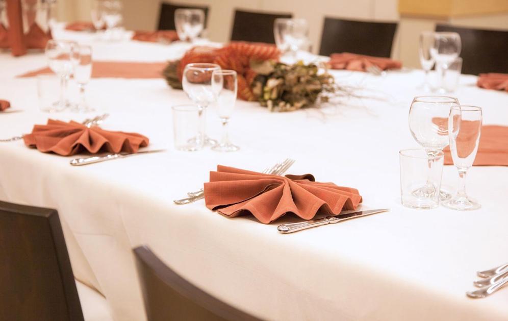 Banquet table set with a white tablecloth, folded rust-colored napkins, glassware, and a floral centerpiece.
