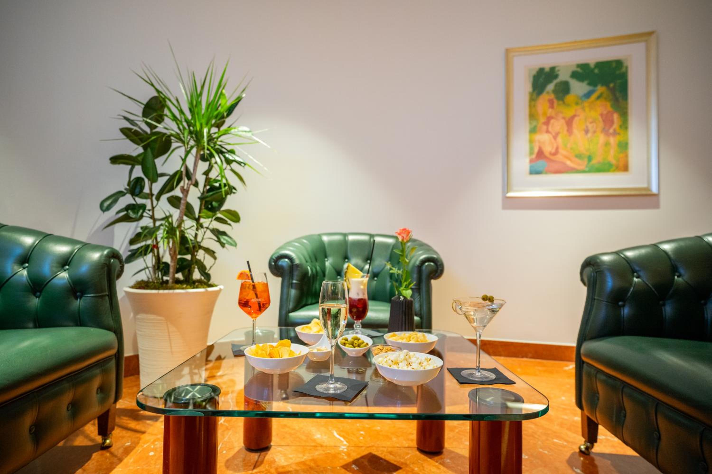 Cocktails and snacks on a glass coffee table between tufted dark green leather armchairs.