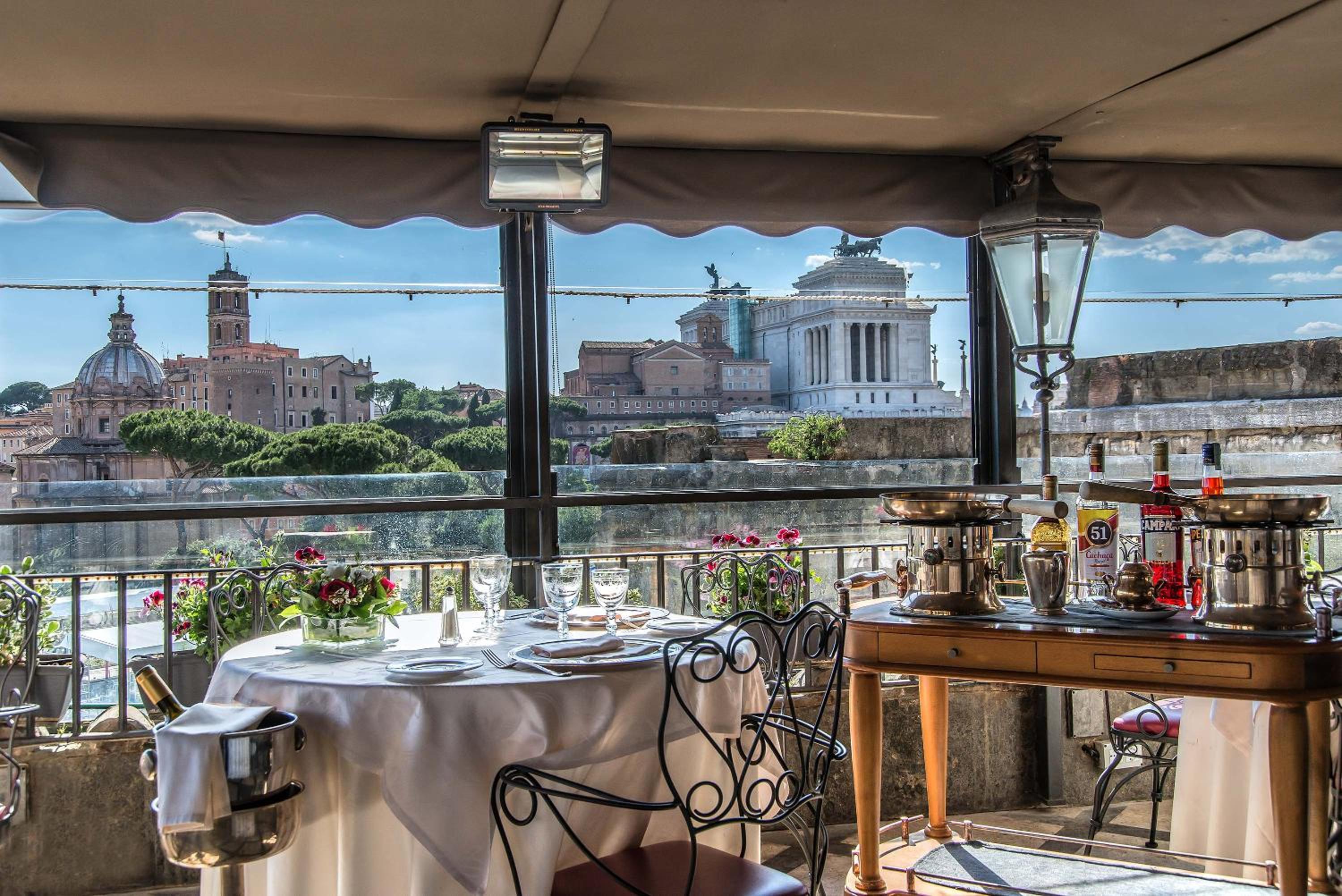 A dining table on a covered terrace overlooking Rome's historic skyline and ancient stone monuments.