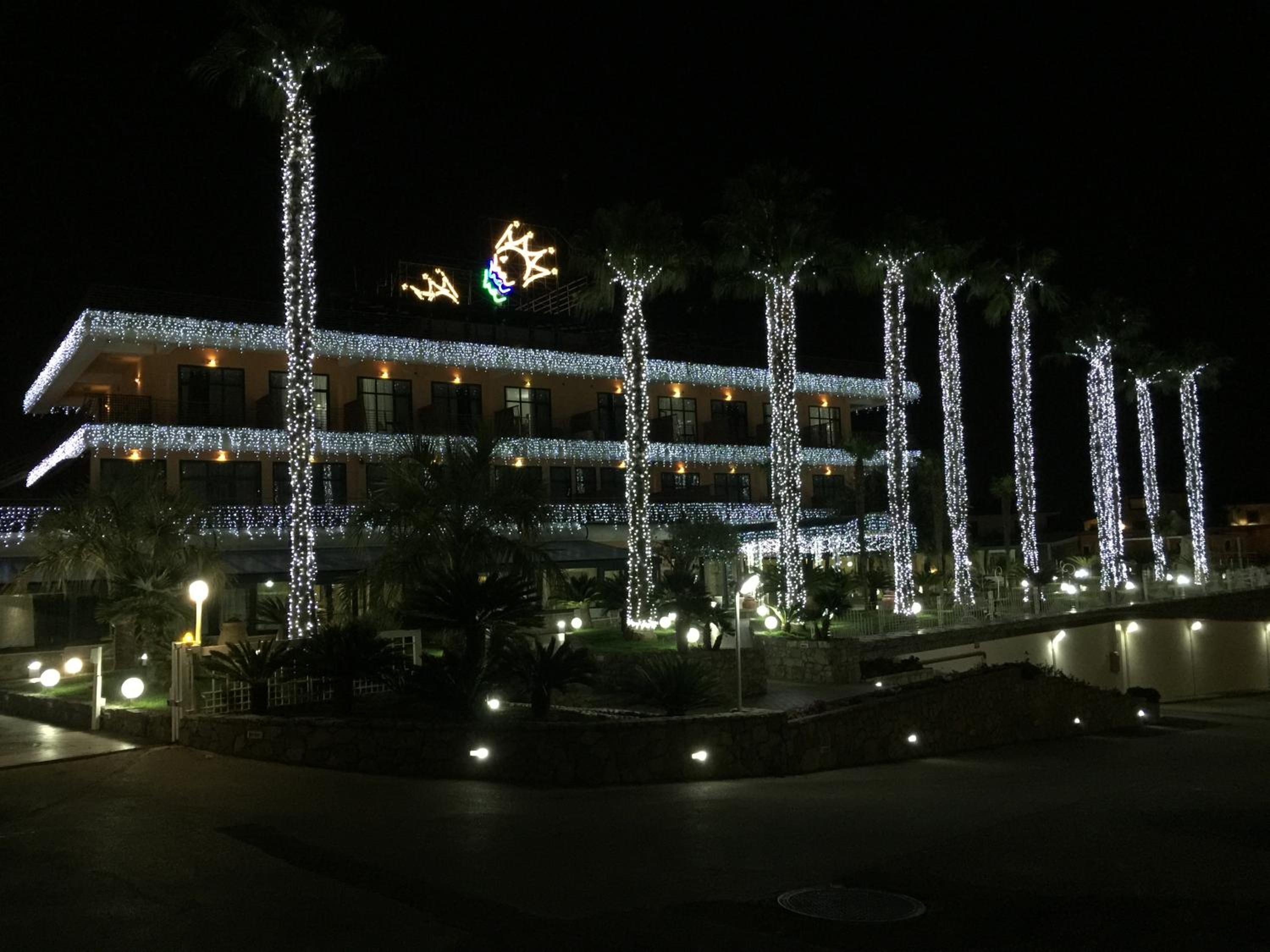 Hotel Gli Dei exterior at night, with palm tree trunks and balconies covered in fairy lights.