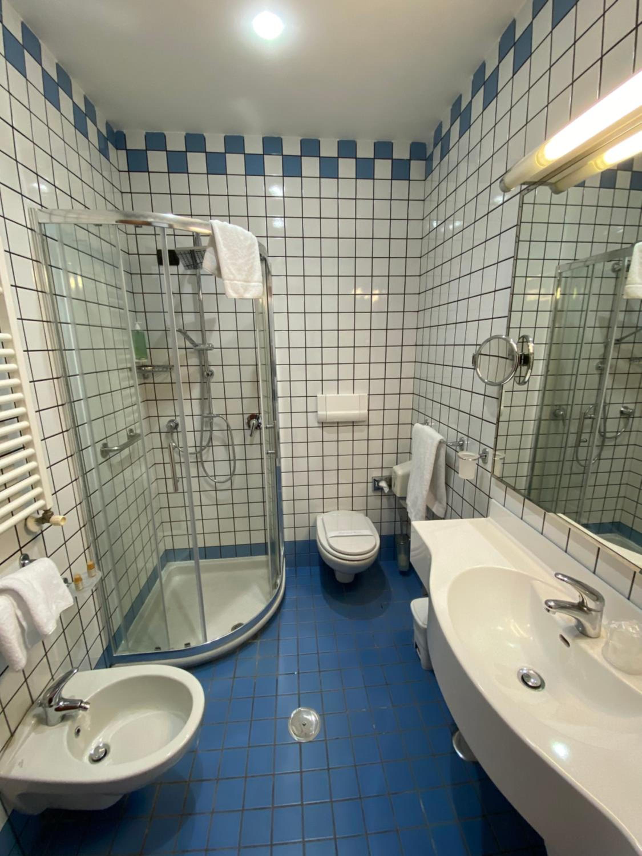 Bathroom with blue floor tiles, white grid wall tiles, corner glass shower, and white vanity.