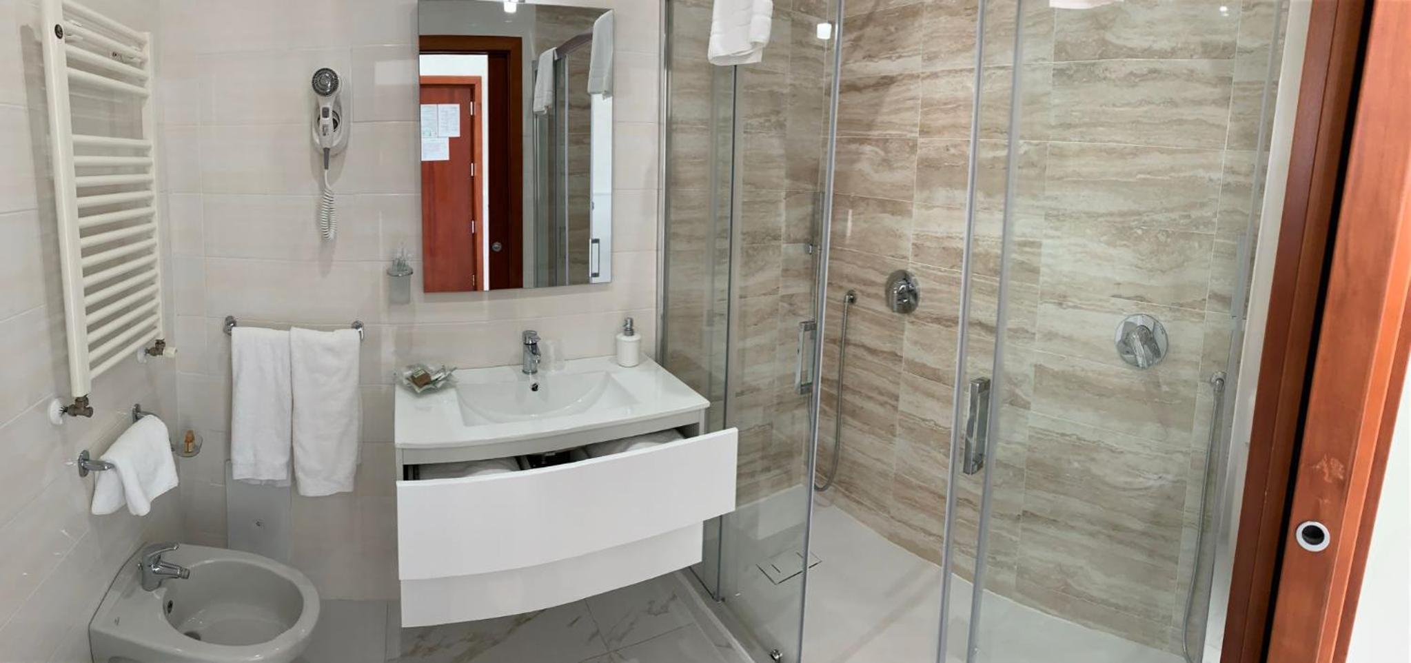 Bathroom with beige stone tiles in a glass shower stall, floating white vanity, and bidet.