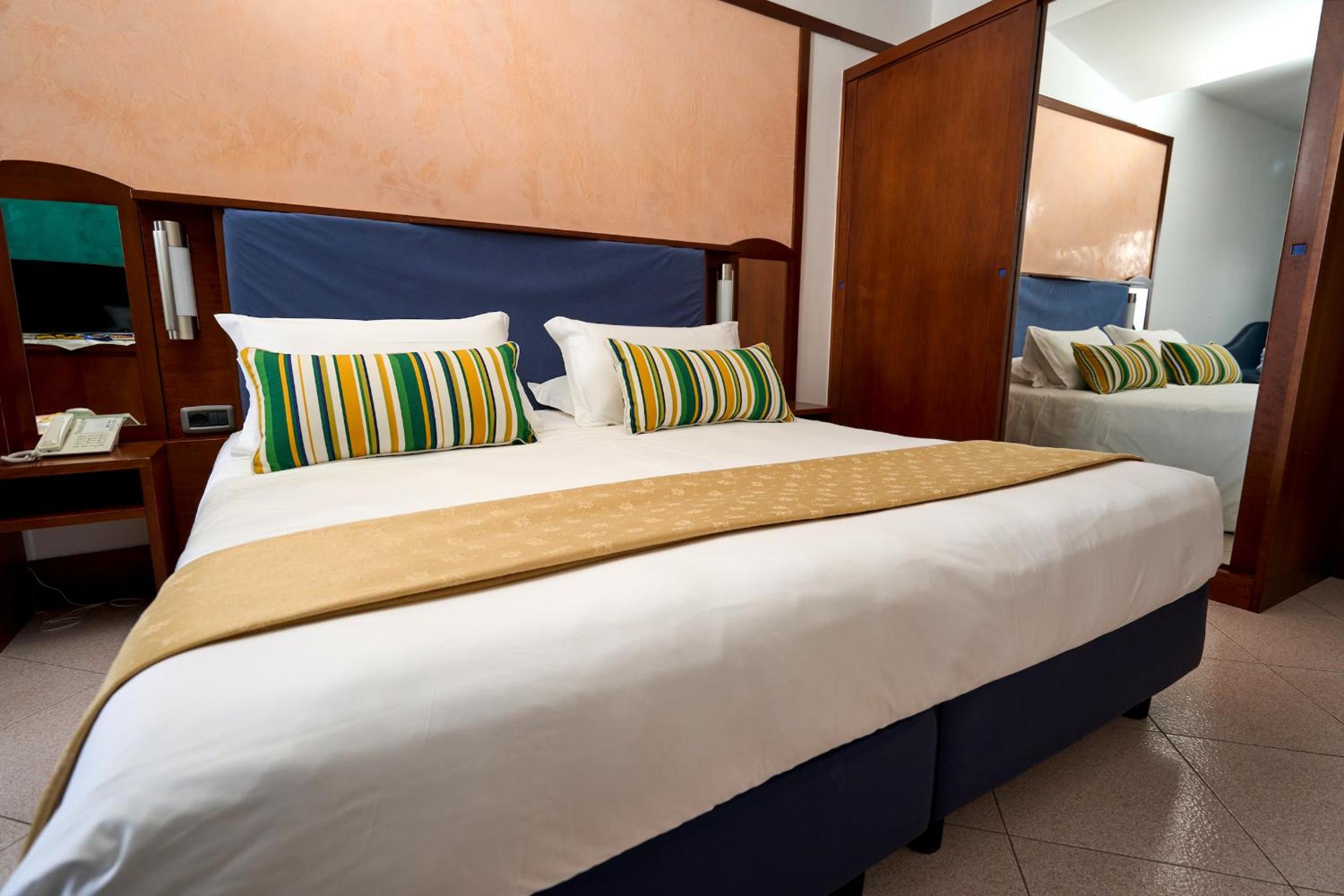 A bedroom at Hotel Graal with a large bed, striped accent pillows, and wooden wardrobes.