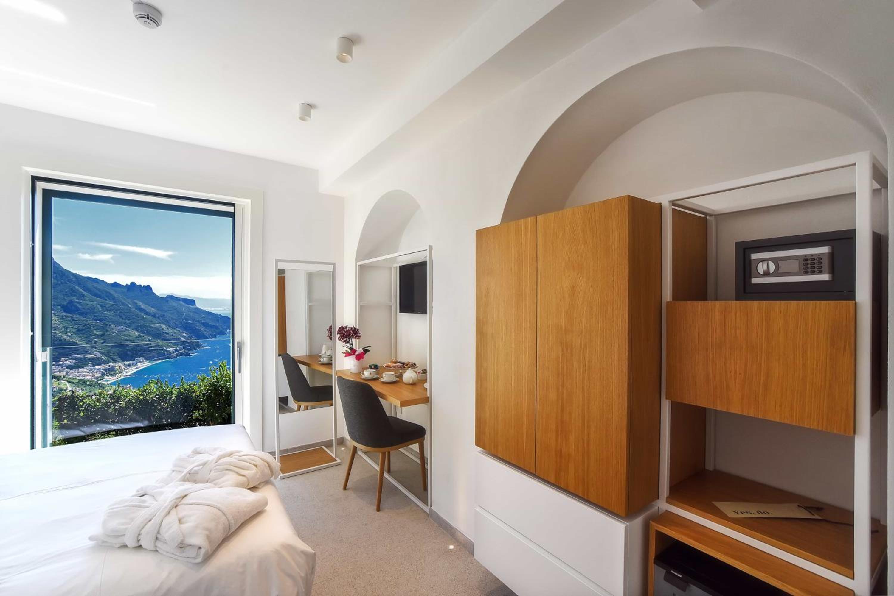 A bright bedroom with an arched ceiling alcove, wooden cabinets, and a window framing the coastline.