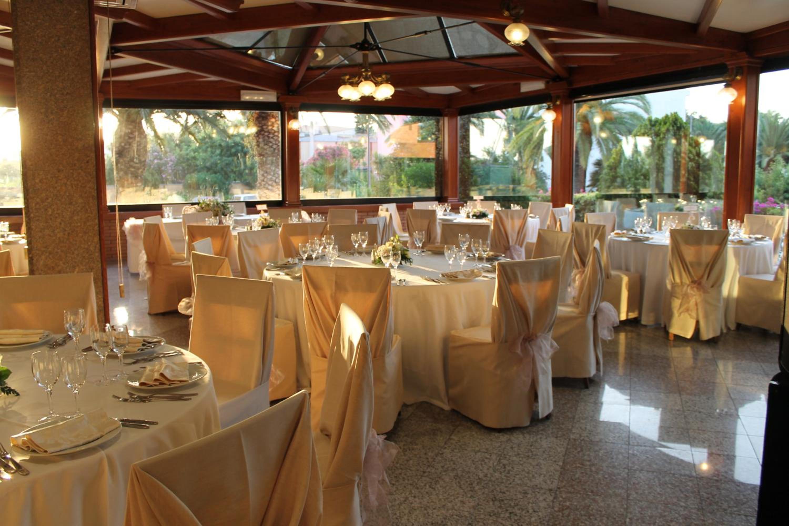 A dining room with round tables set with formal linens and glassware beneath a timber-beamed ceiling.