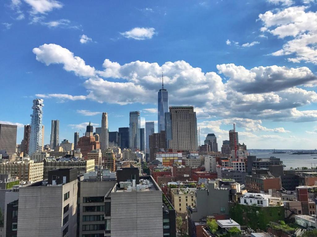 High-angle view overlooking the Manhattan skyline with skyscrapers and the Hudson River under partly cloudy skies.