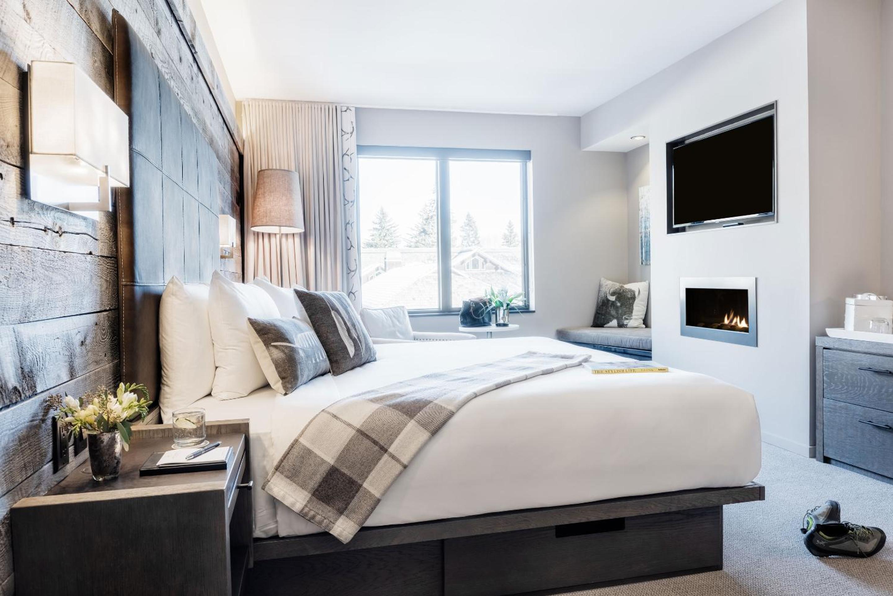 A bedroom featuring a bed against a weathered wood wall, an in-wall fireplace below a TV, and a window.